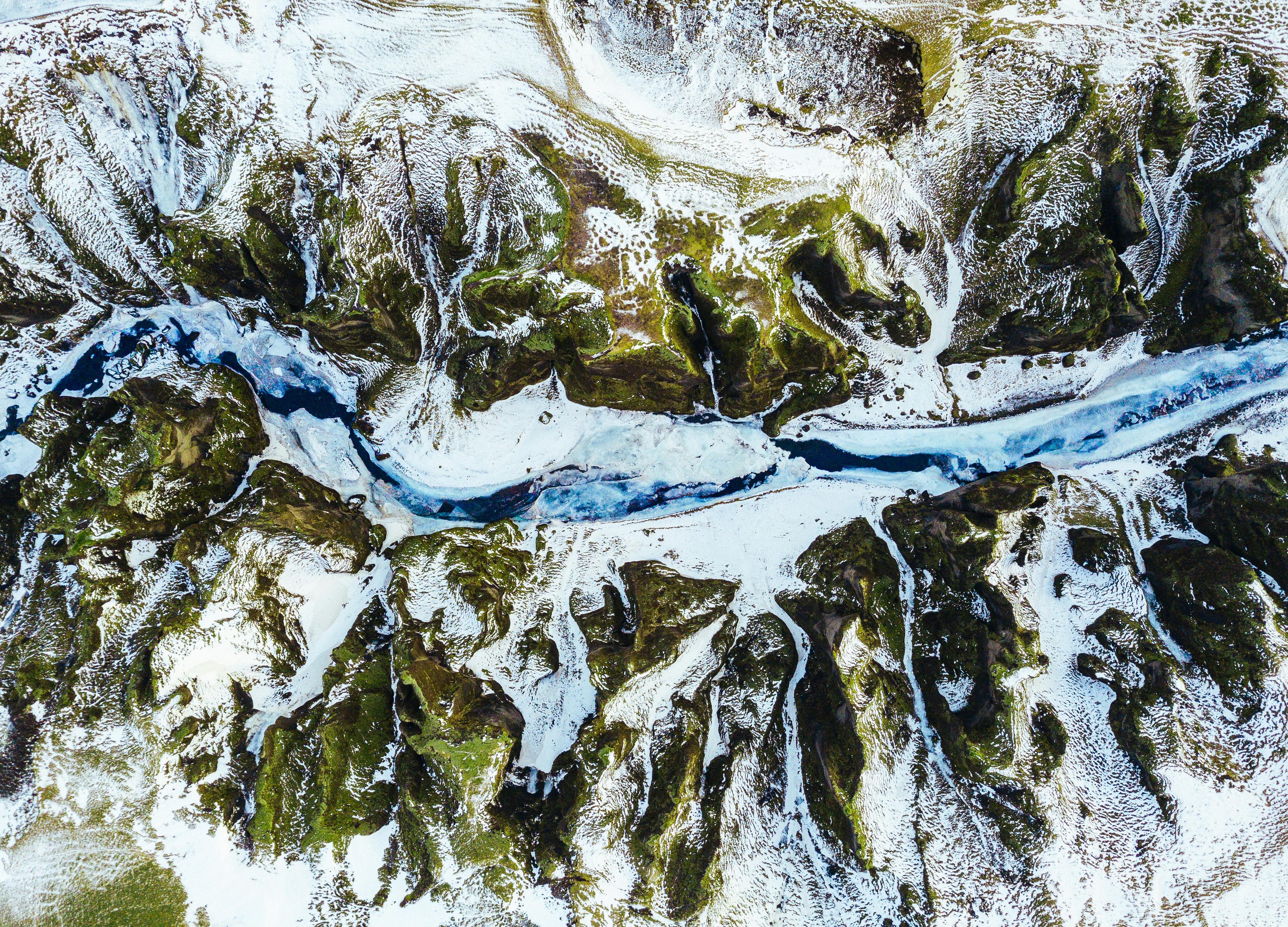 Aerial view of a winding river cutting through a snow-dusted, mossy landscape, showcasing a contrast of vibrant blue water against the earthy tones of the terrain.