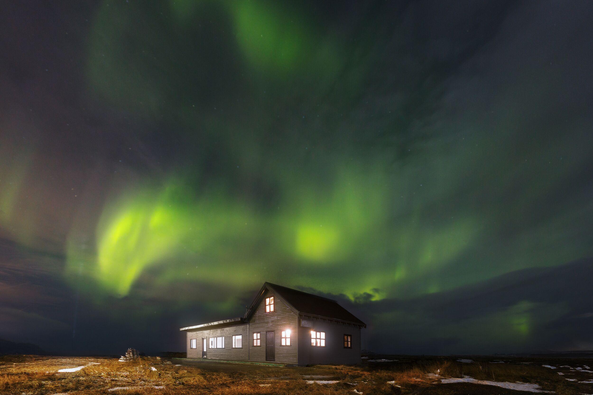 A house with glowing windows under a vibrant green aurora borealis.