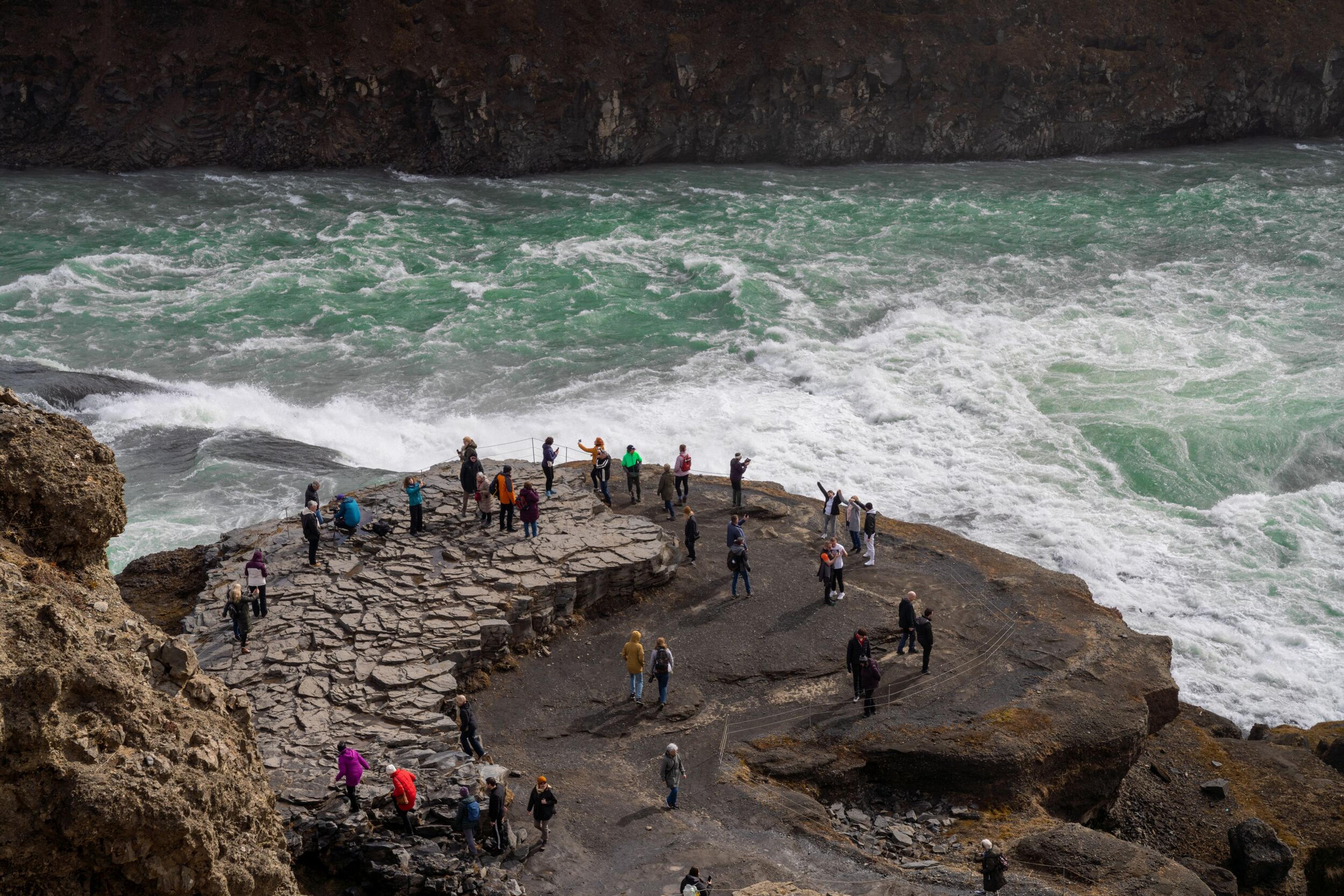 Tourists gathered near the edge of Gullfoss waterfall in Iceland, taking photos and enjoying the powerful, rushing waters.