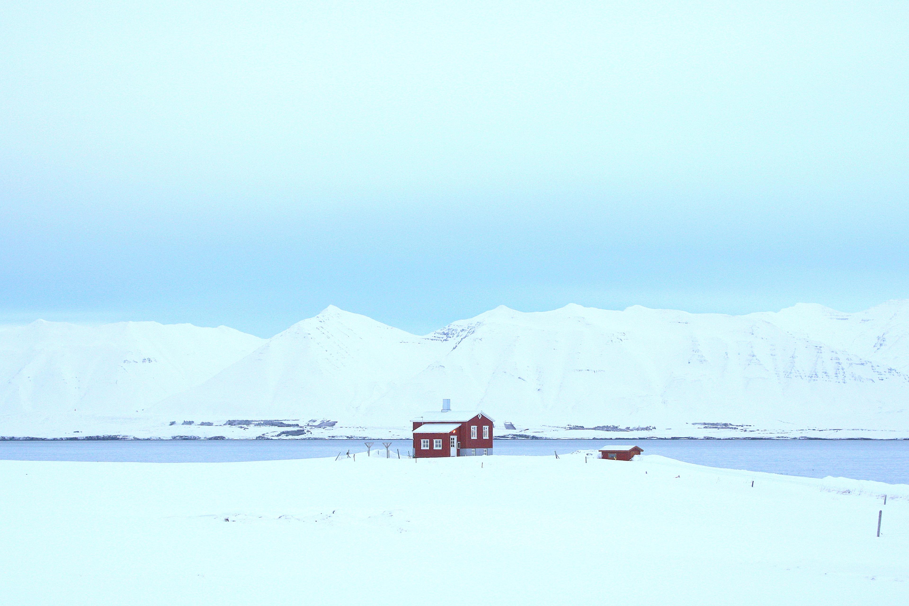 Two charming small red wooden houses nestled in a snowy landscape by the side of a serene sea fjord.