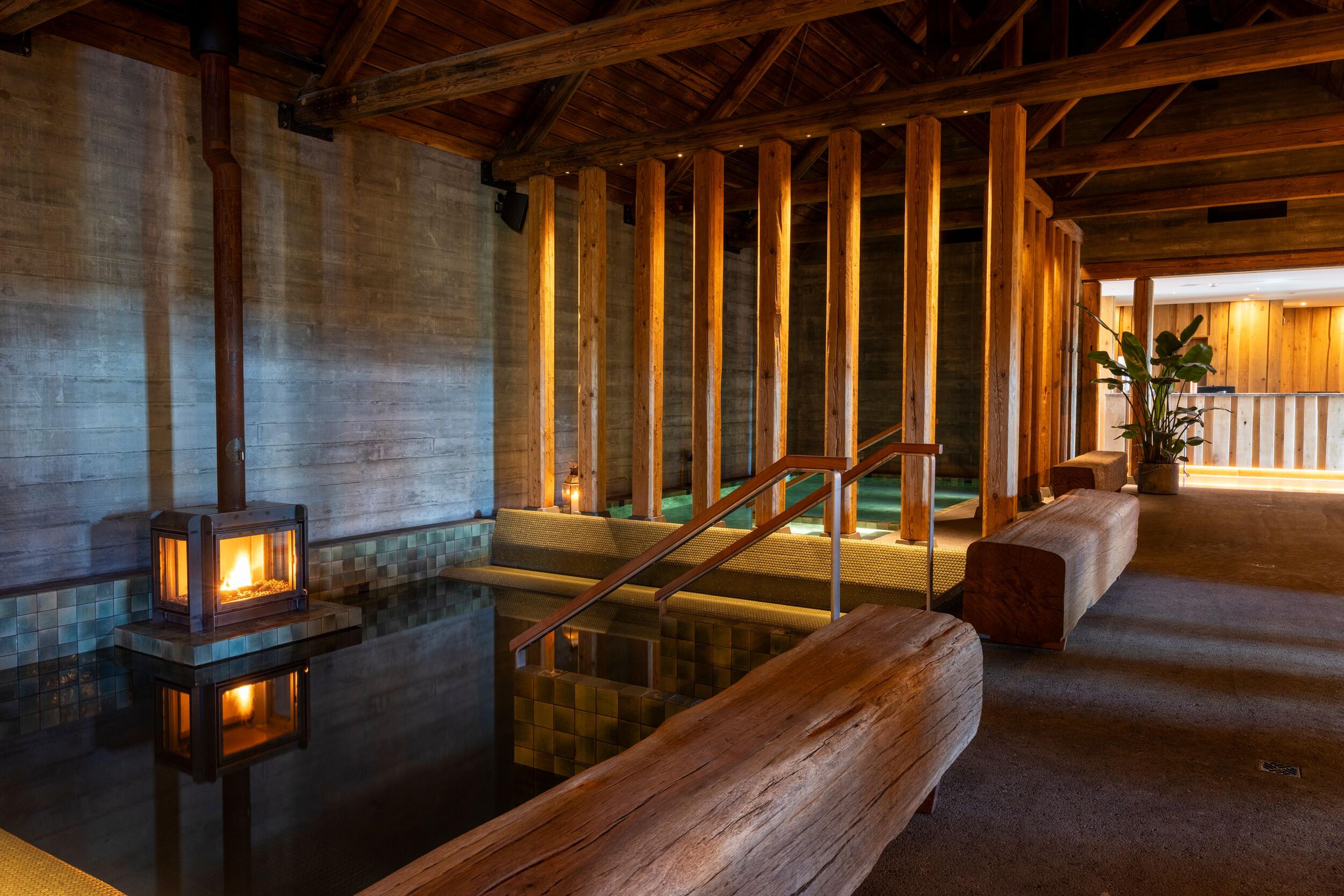 An indoor spa area with a dark pool, a modern fireplace, and exposed wooden beams.