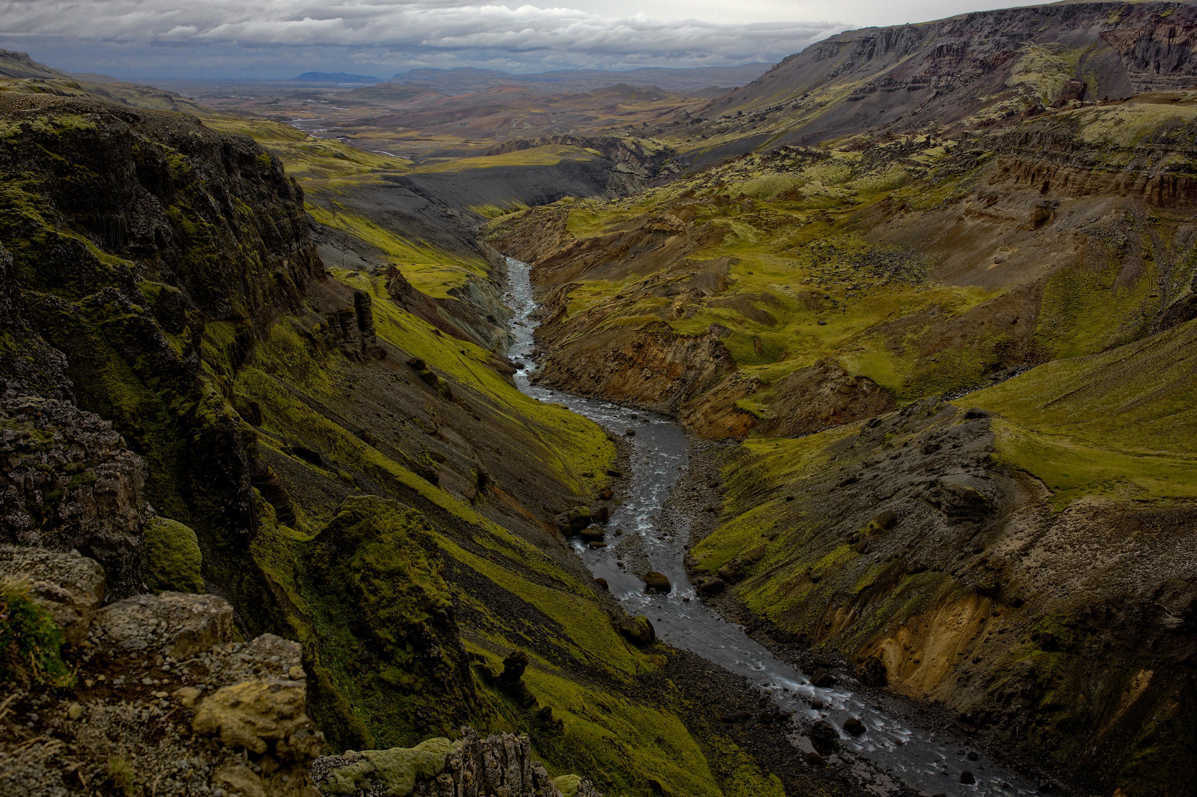 A winding river flows through a deep, moss-covered canyon under a cloudy sky.