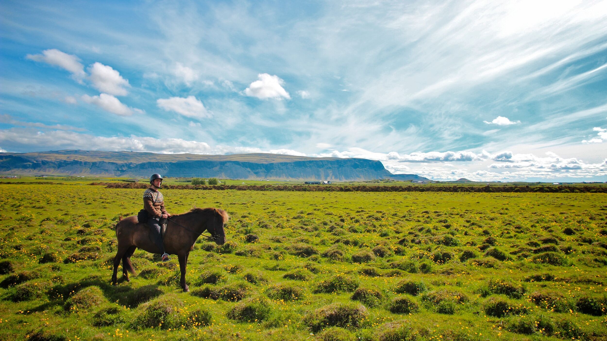 A person on horseback riding through a sunlit green meadow