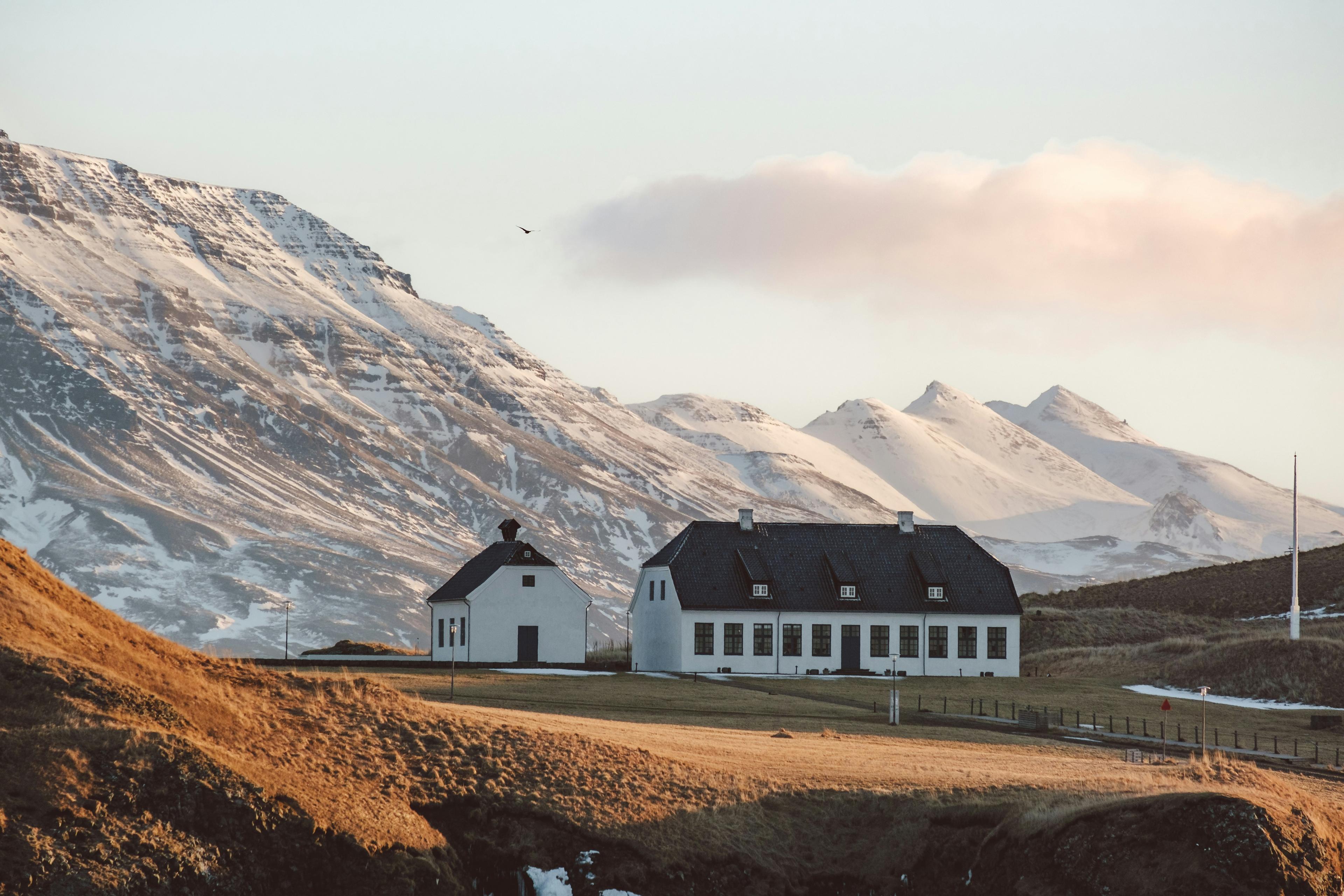 Snow-capped mountains in the background with traditional white houses on rolling golden fields bathed in soft sunlight.