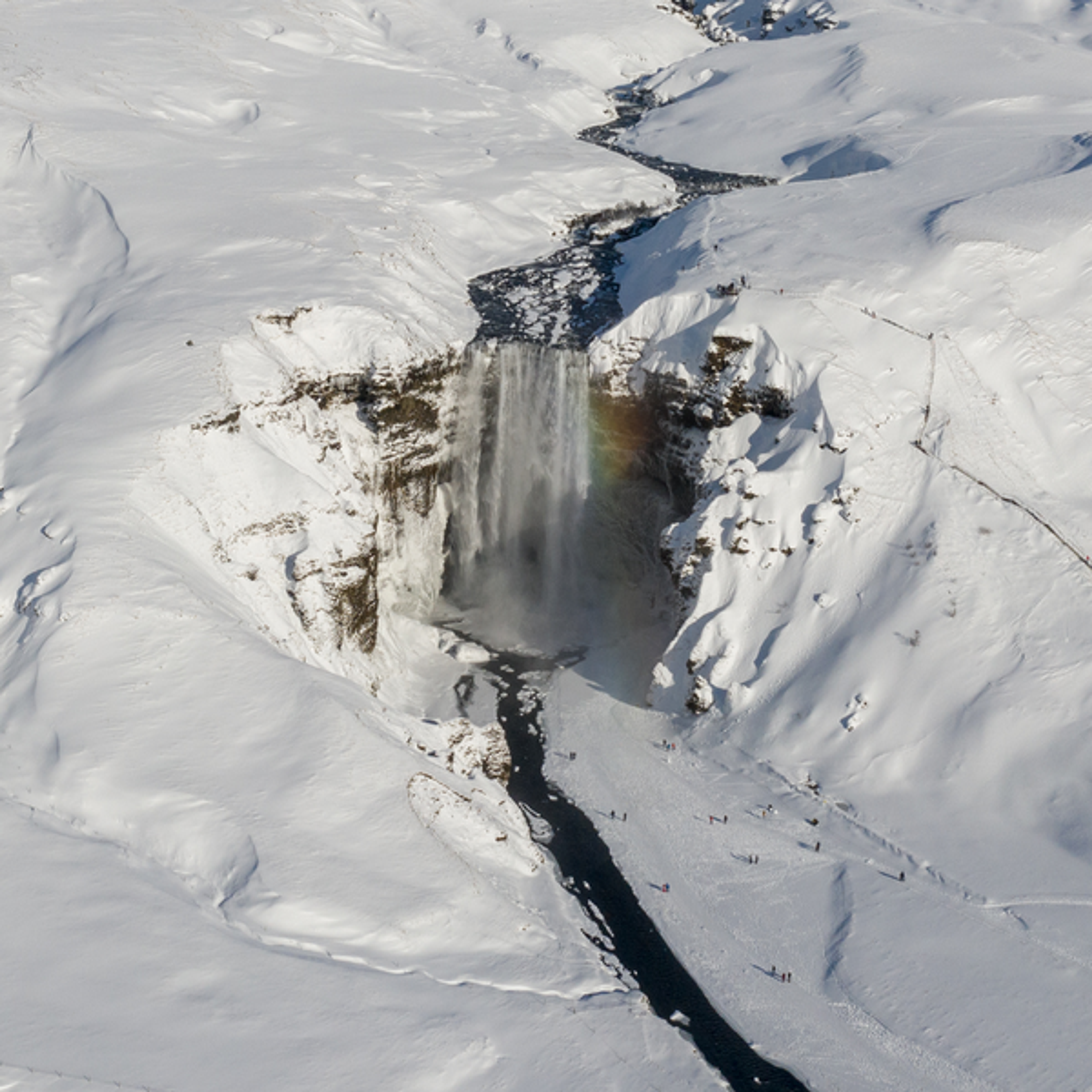 Aerial perspective of Skogafoss waterfall during winter, enveloped by a pristine snowy landscape.