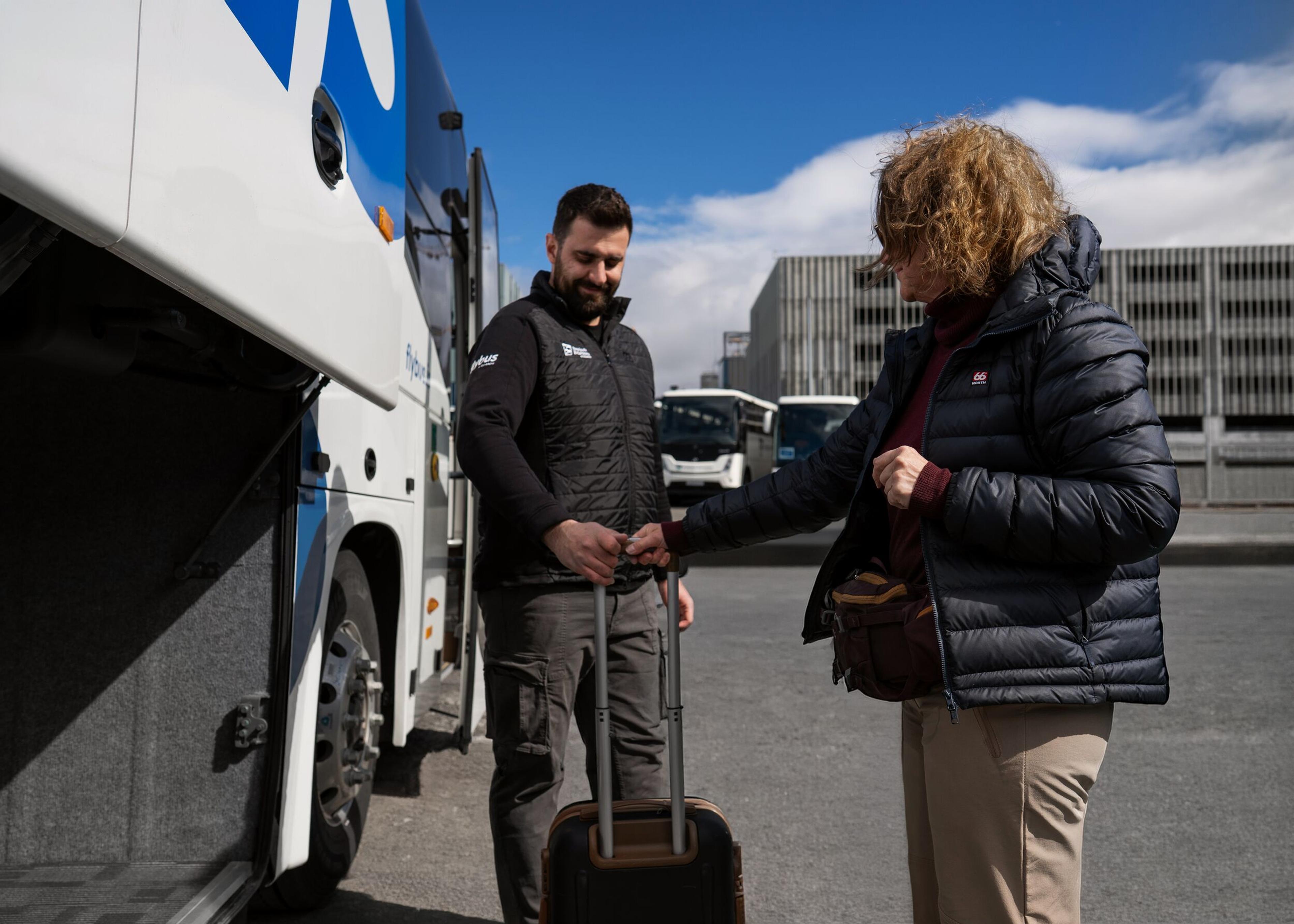 A bus employee takes a suitcase from a passenger next to a bus with an open luggage compartment.