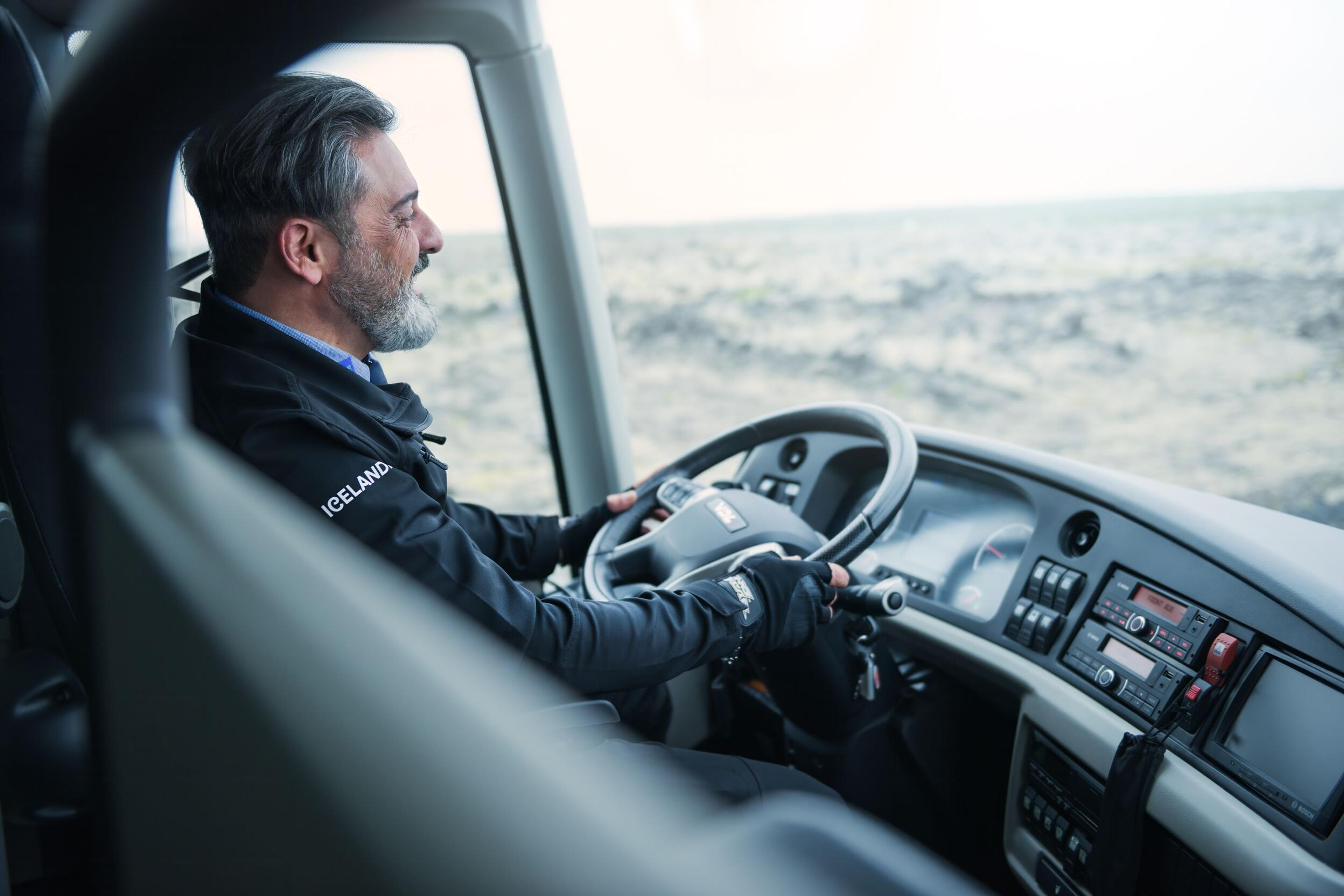 A bus driver, focused and driving, with a dashboard view from the passenger's perspective.