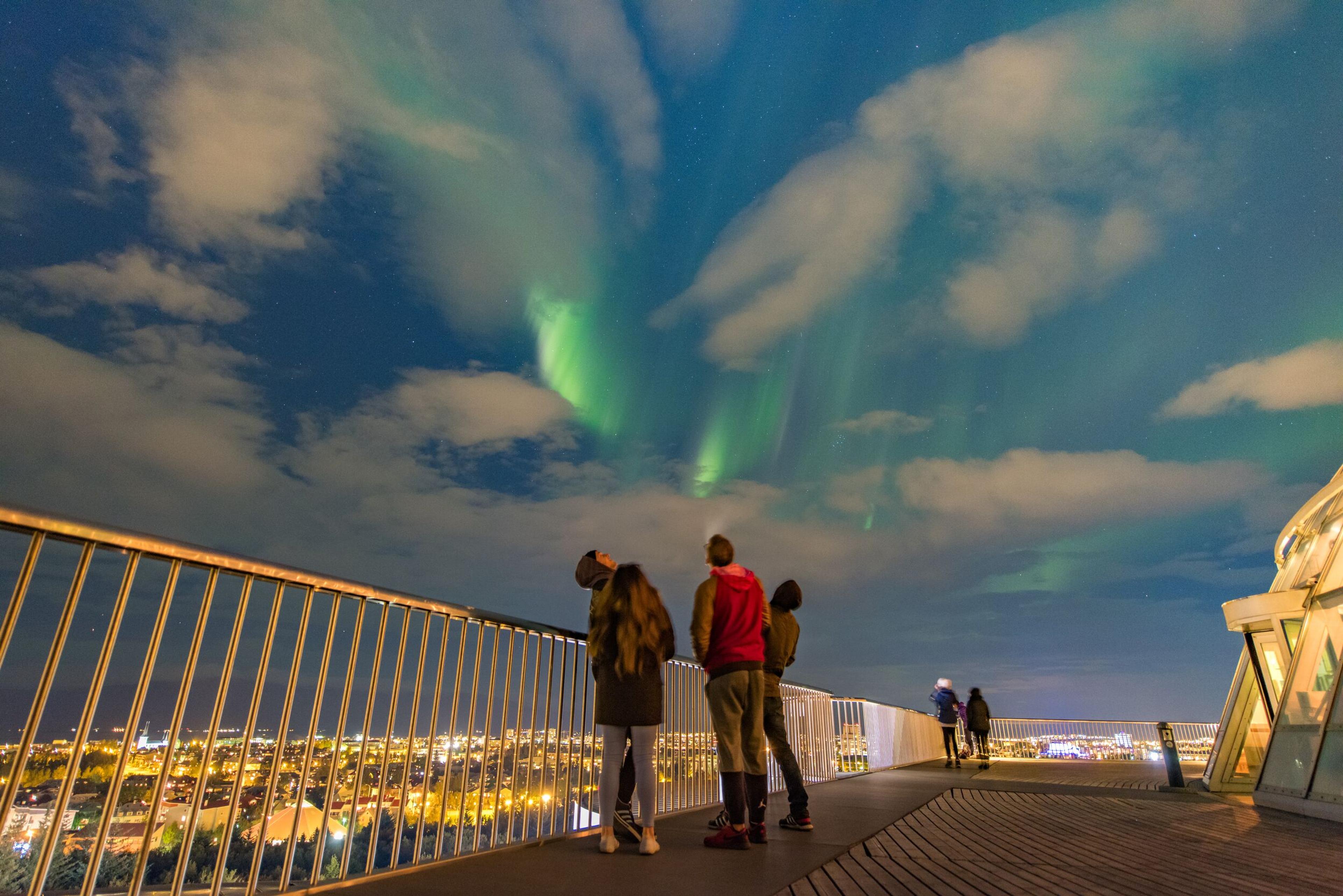  Tourists at Perlan Observatory in Reykjavik, Iceland, admire the Northern Lights from an elevated platform under a starry night sky.