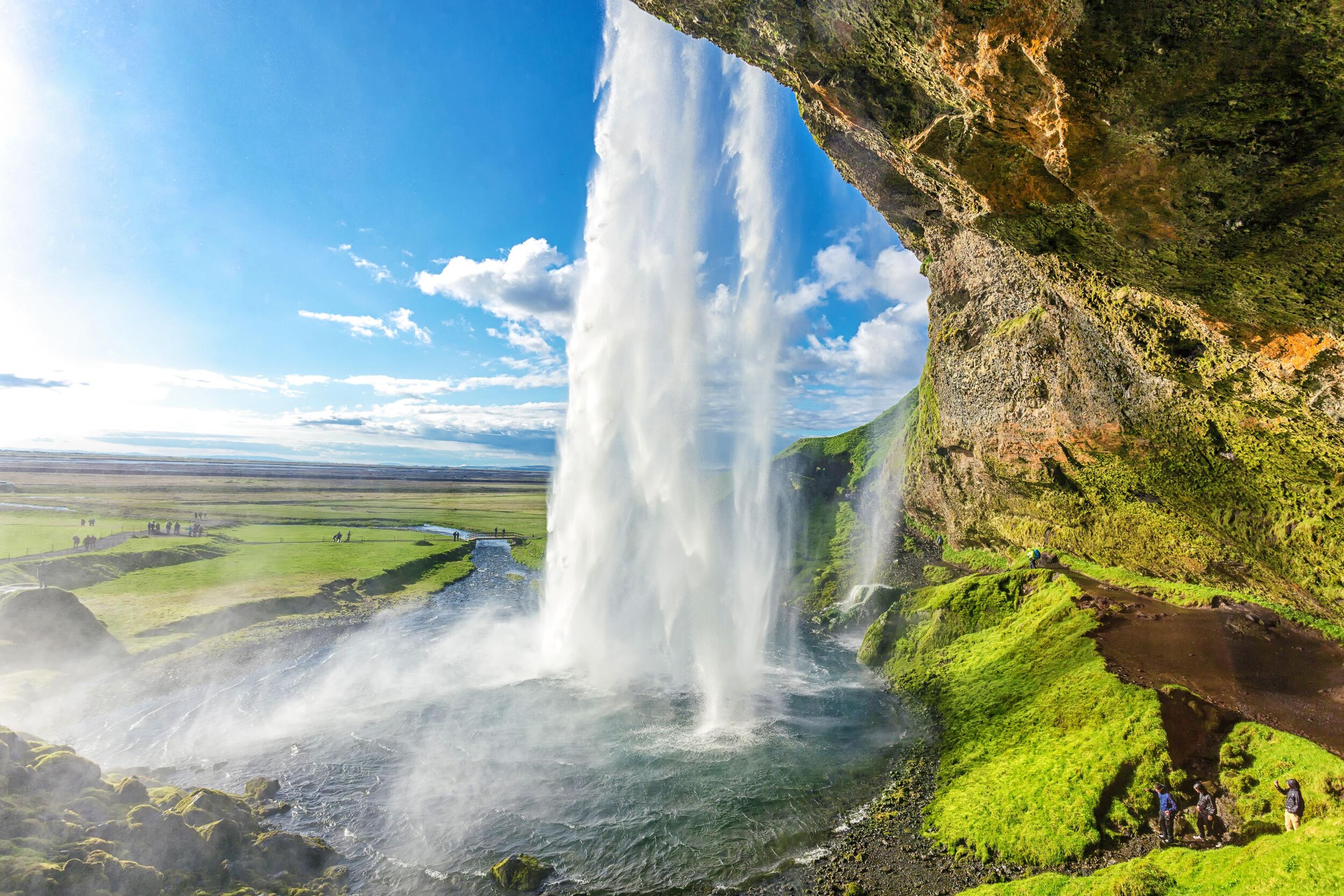 a waterfall is coming down a cliff in the middle of a field .