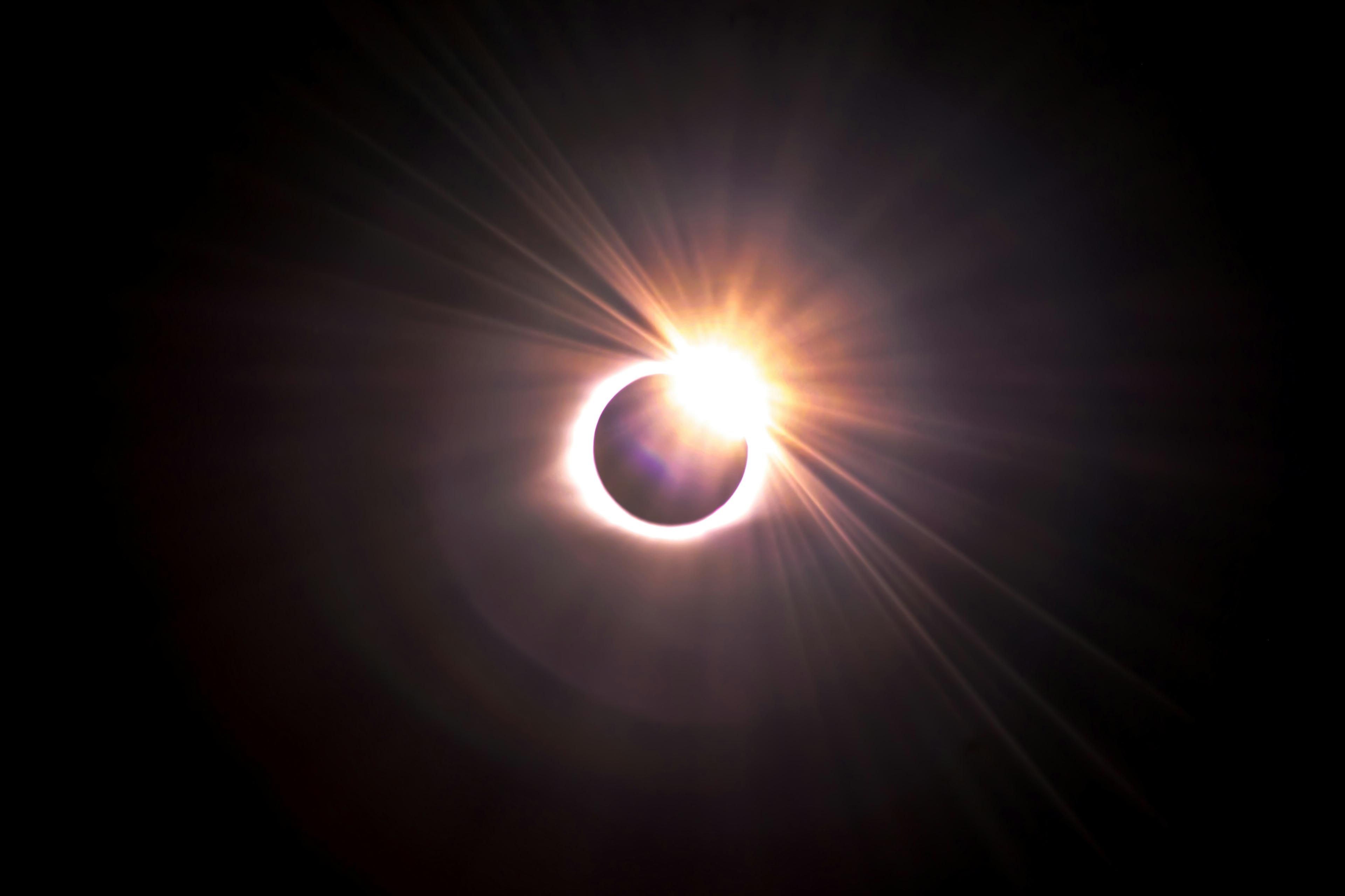 A total solar eclipse with the sun's corona visible, showing a bright ring of light surrounding the darkened moon, set against a dark sky.