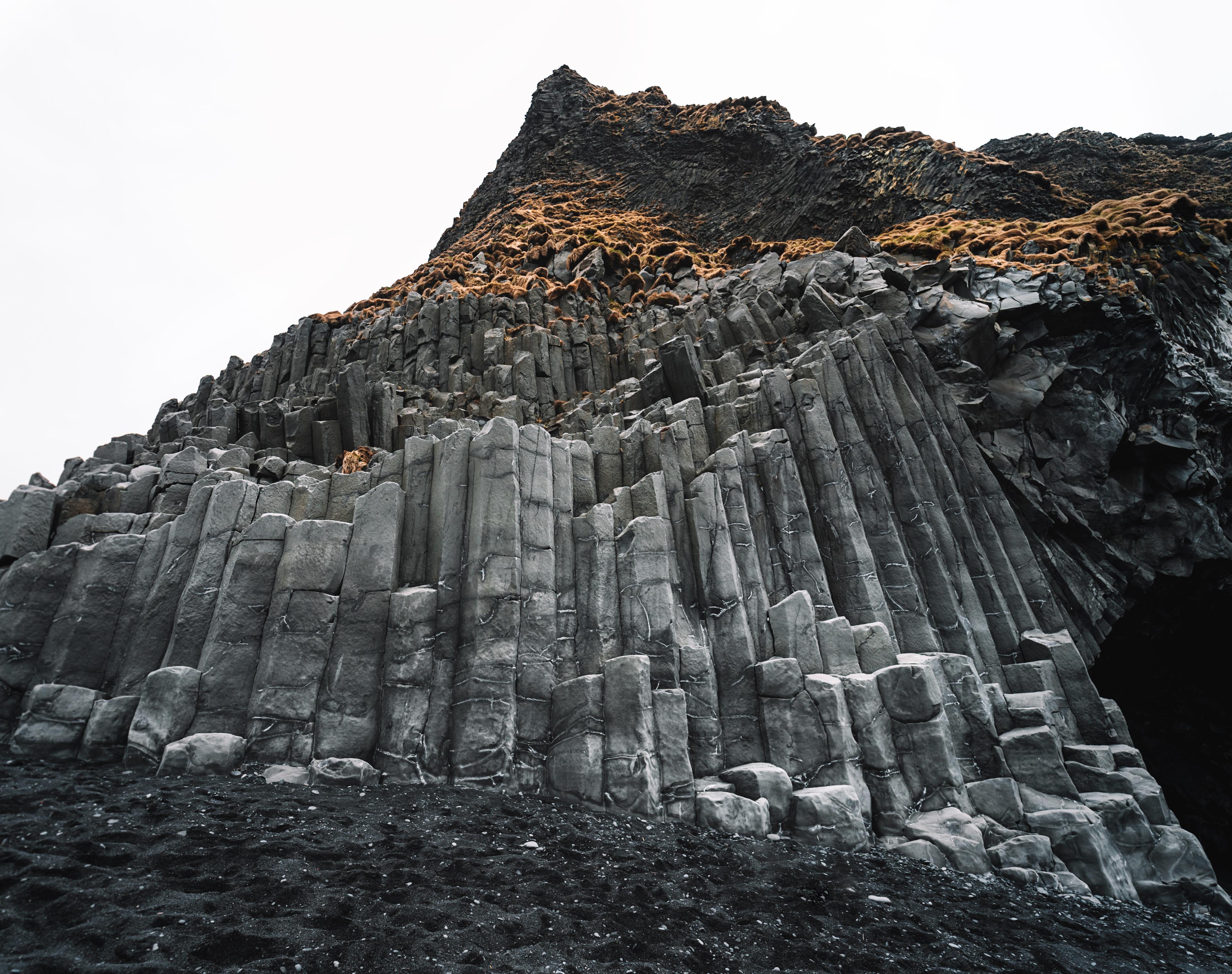 Columnar basalt formations creating a natural wall with a cave at the base, against a black sand beach.