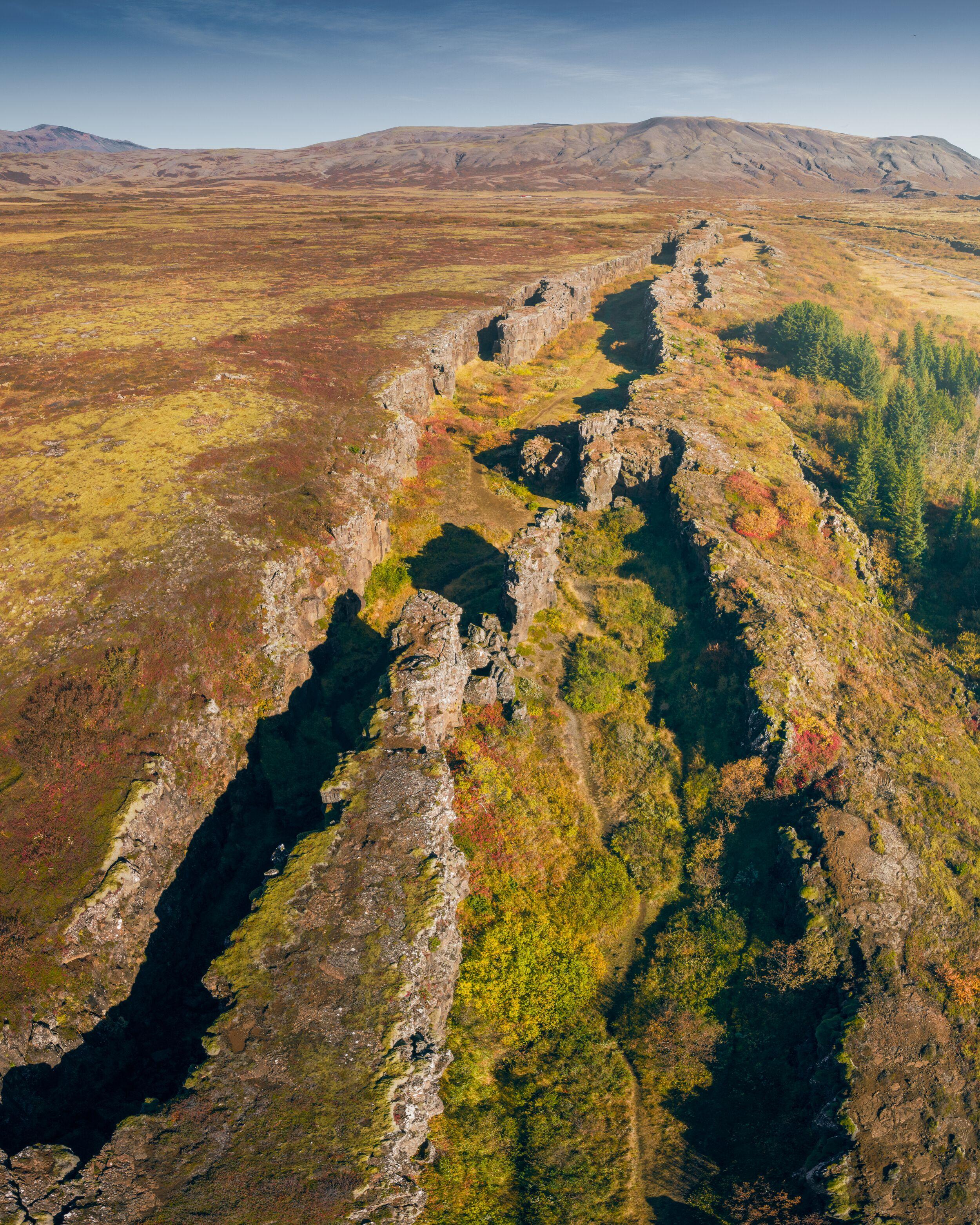 Aerial view of the dramatic tectonic rift at Thingvellir National Park, Iceland, showcasing rugged terrain and sparse vegetation.