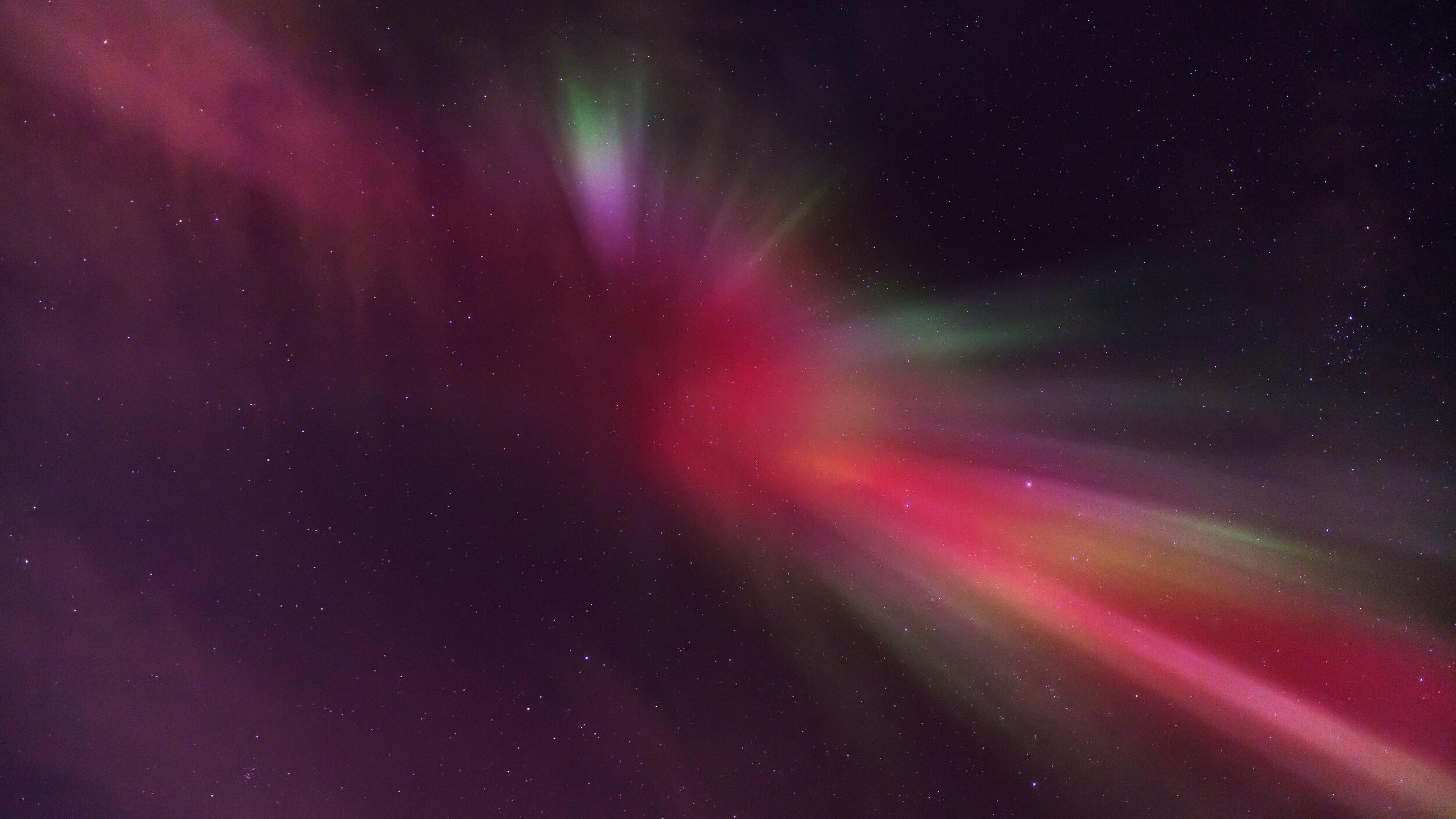 A vibrant display of Northern Lights in the night sky, showcasing a spectrum of green, red, and purple hues.