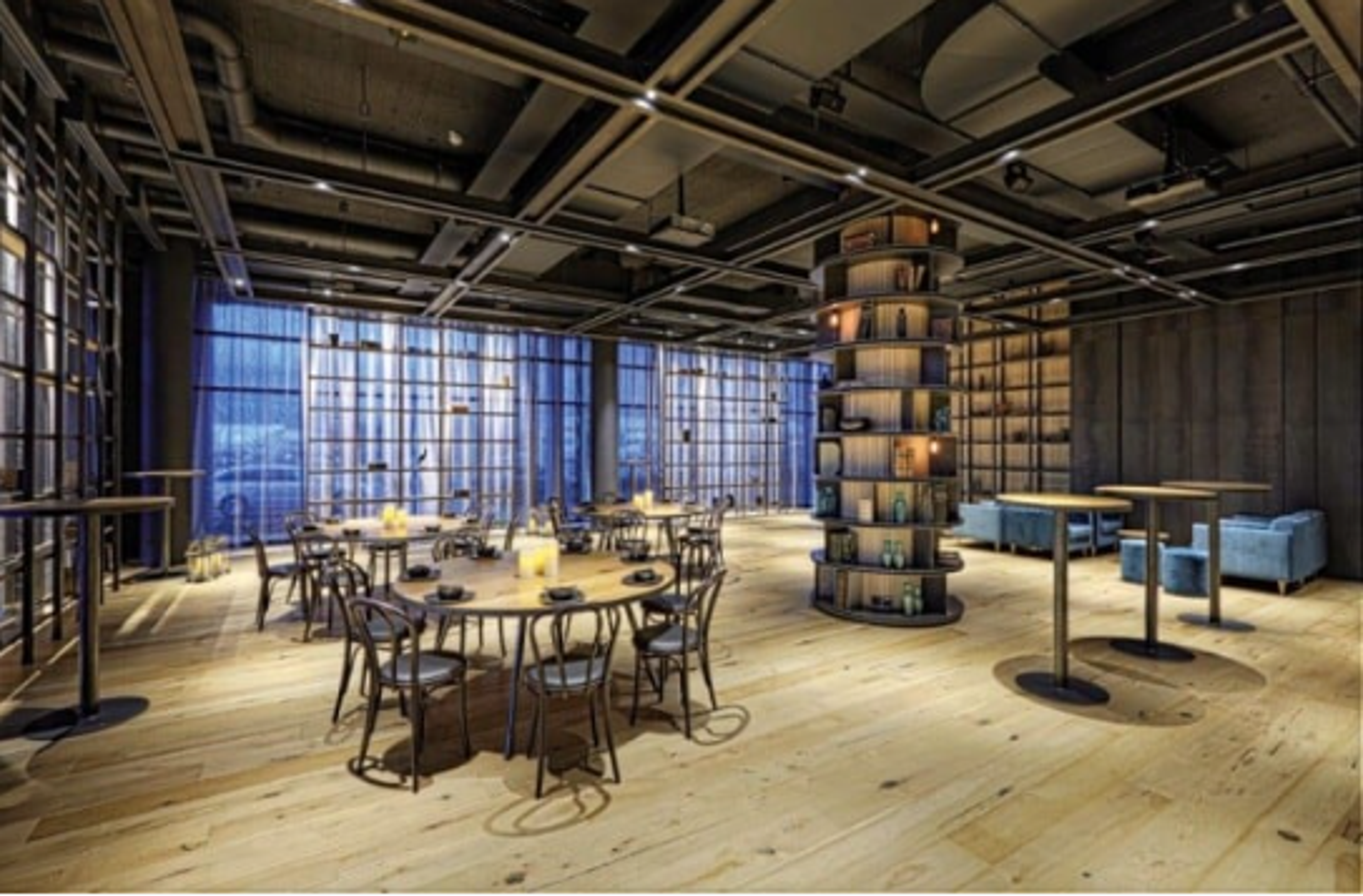 Modern lounge area with wooden floors, circular shelving, and ambient lighting, featuring tables and chairs arranged for casual seating.