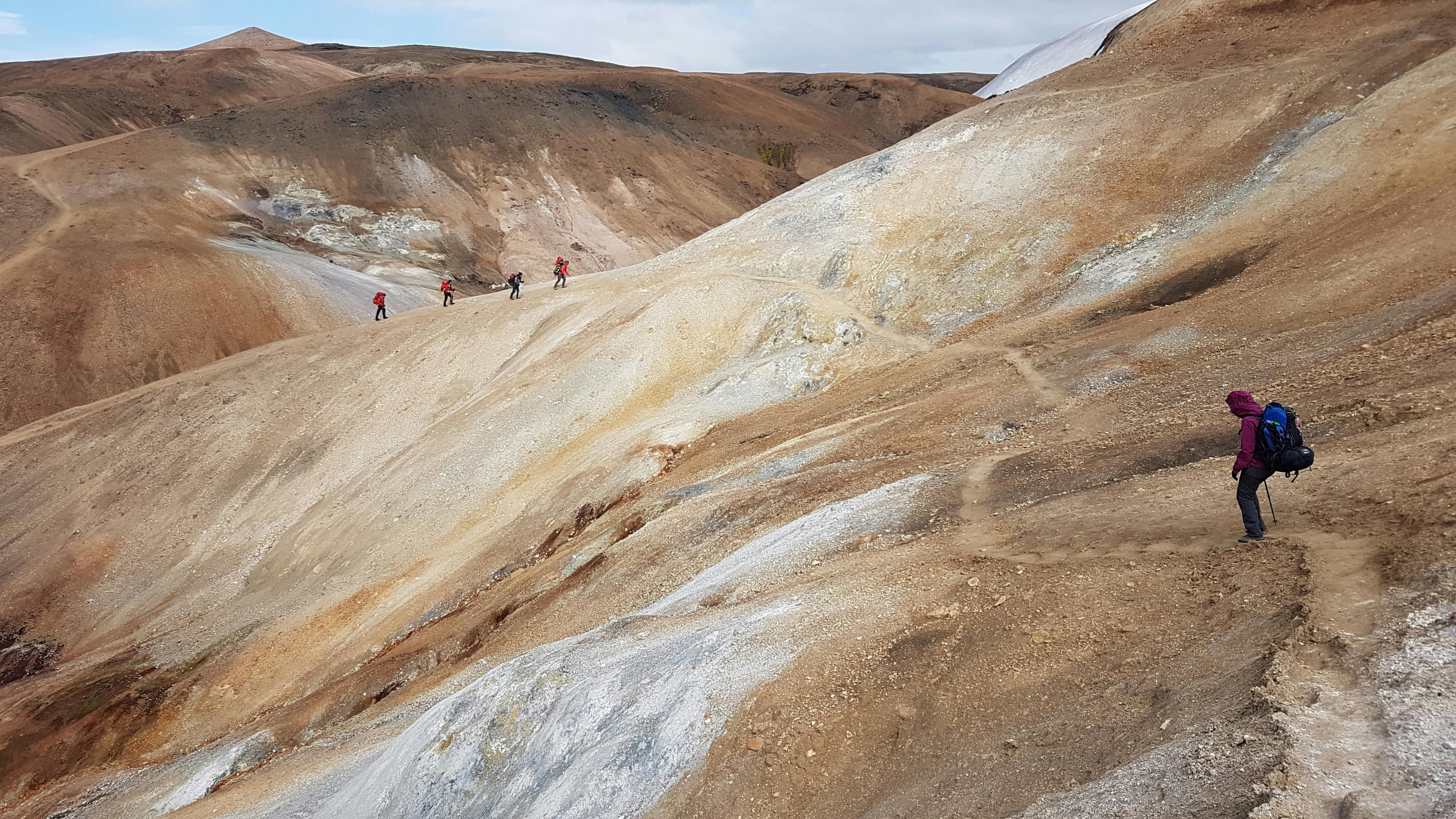 Hikers trekking across a barren, rocky landscape in the Icelandic Highlands, showcasing the rugged terrain and adventure.