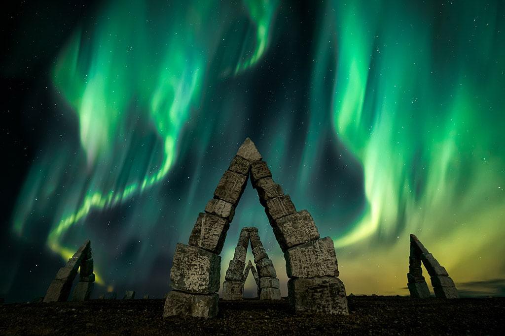 Green aurora borealis over triangular stone structures.