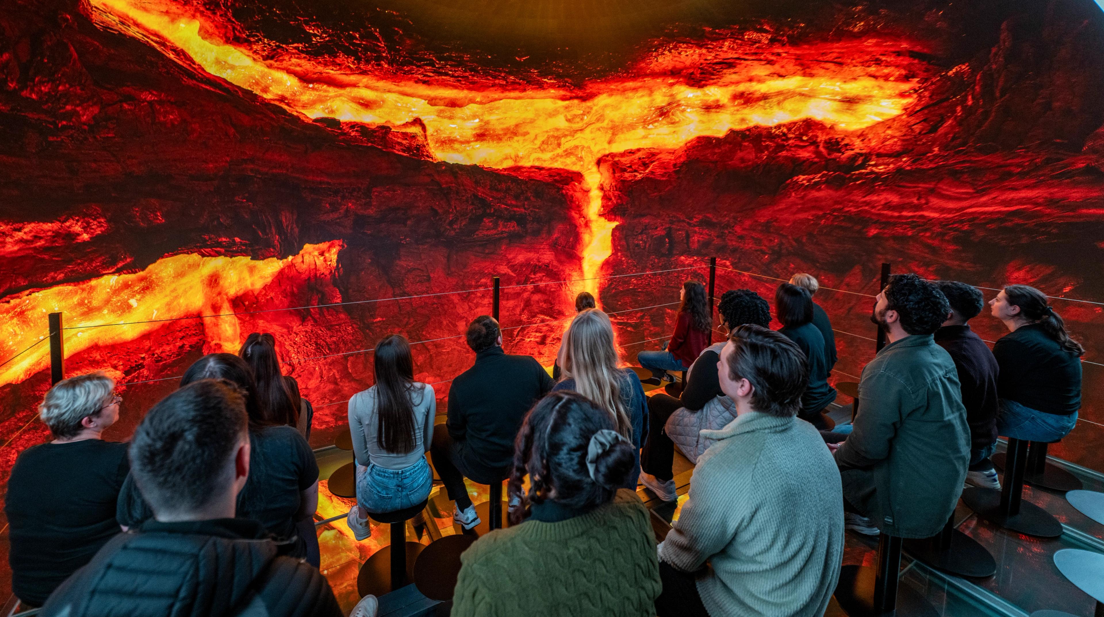 A group watches an immersive exhibit of glowing lava on a large screen.