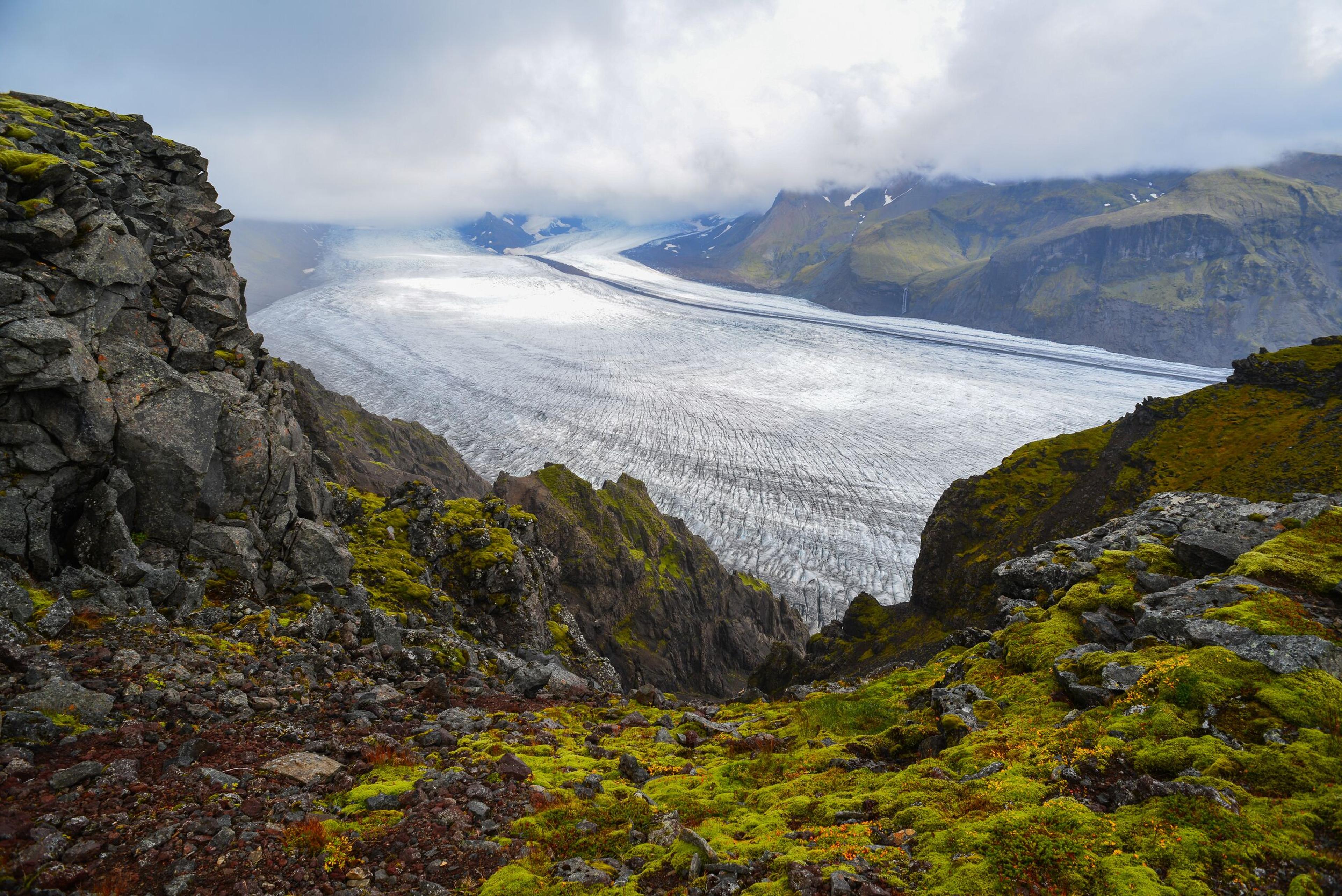"Skaftafellsjökull glacier tongue snaking its way downhill, flanked by rugged, craggy hills, showcasing the raw beauty of Icelandic landscapes.
