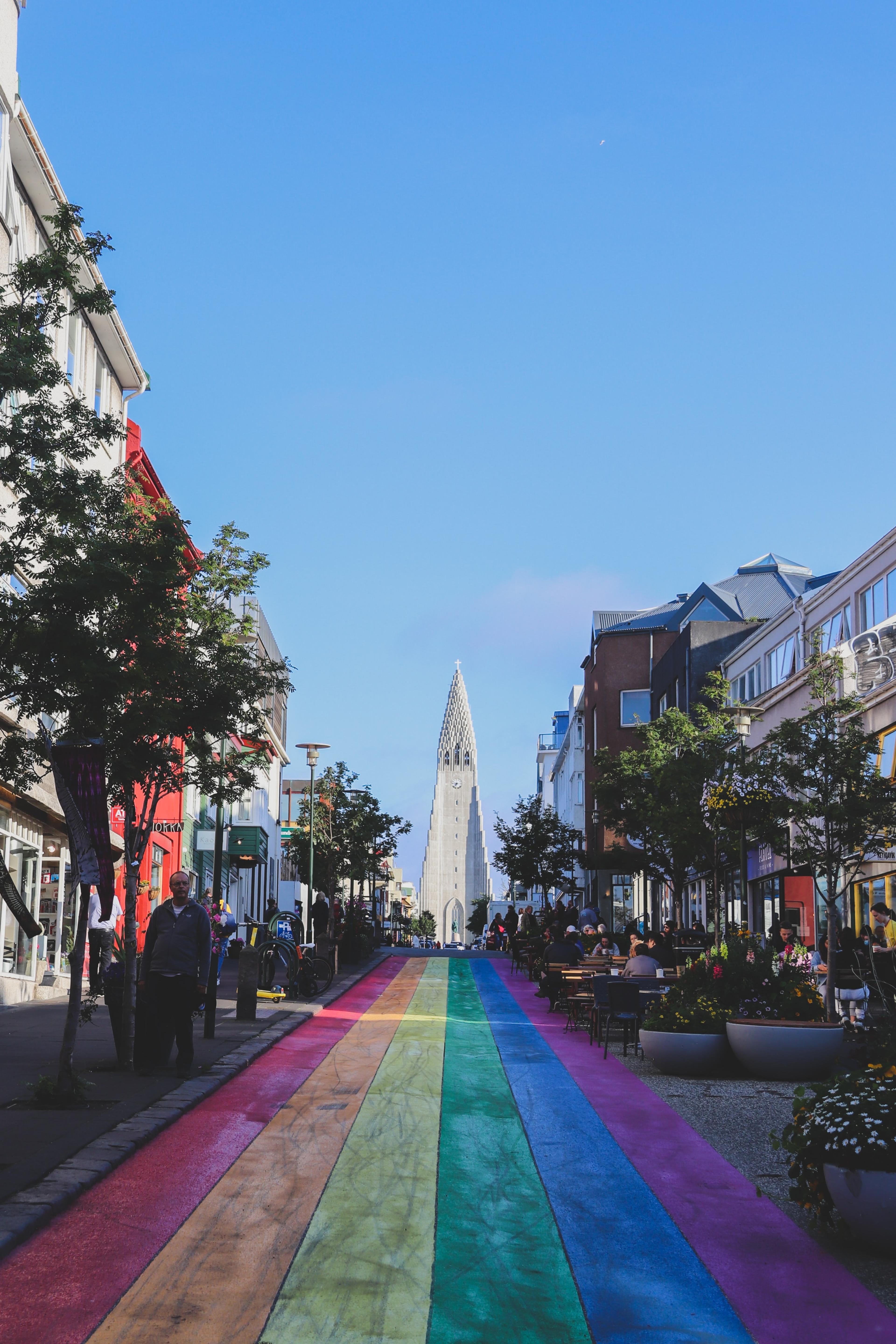 The iconic Rainbow Street in downtown Reykjavík, with the imposing silhouette of Hallgrímskirkja church in the background.
