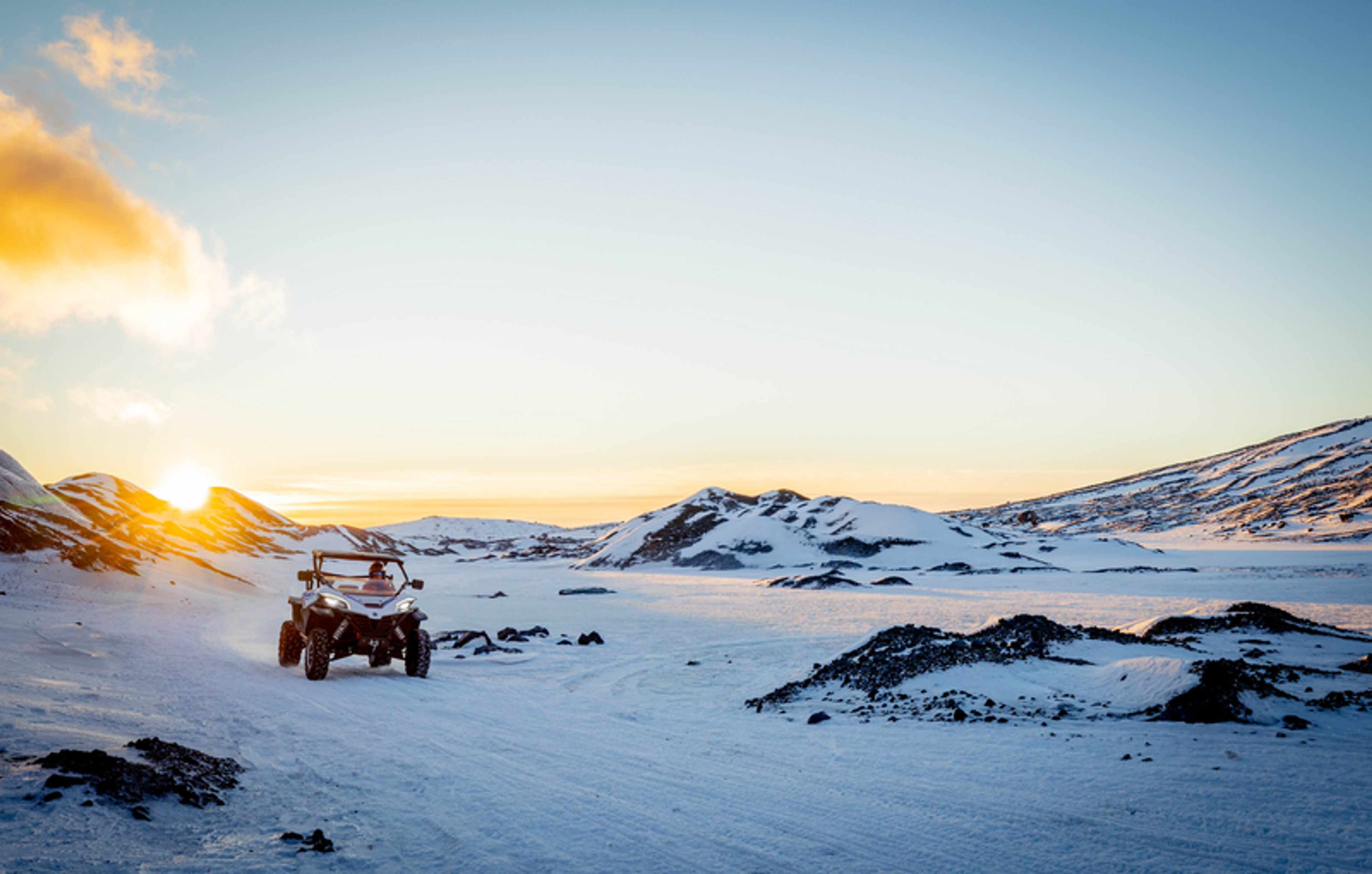 a snowmobile is driving down a snowy road at sunset