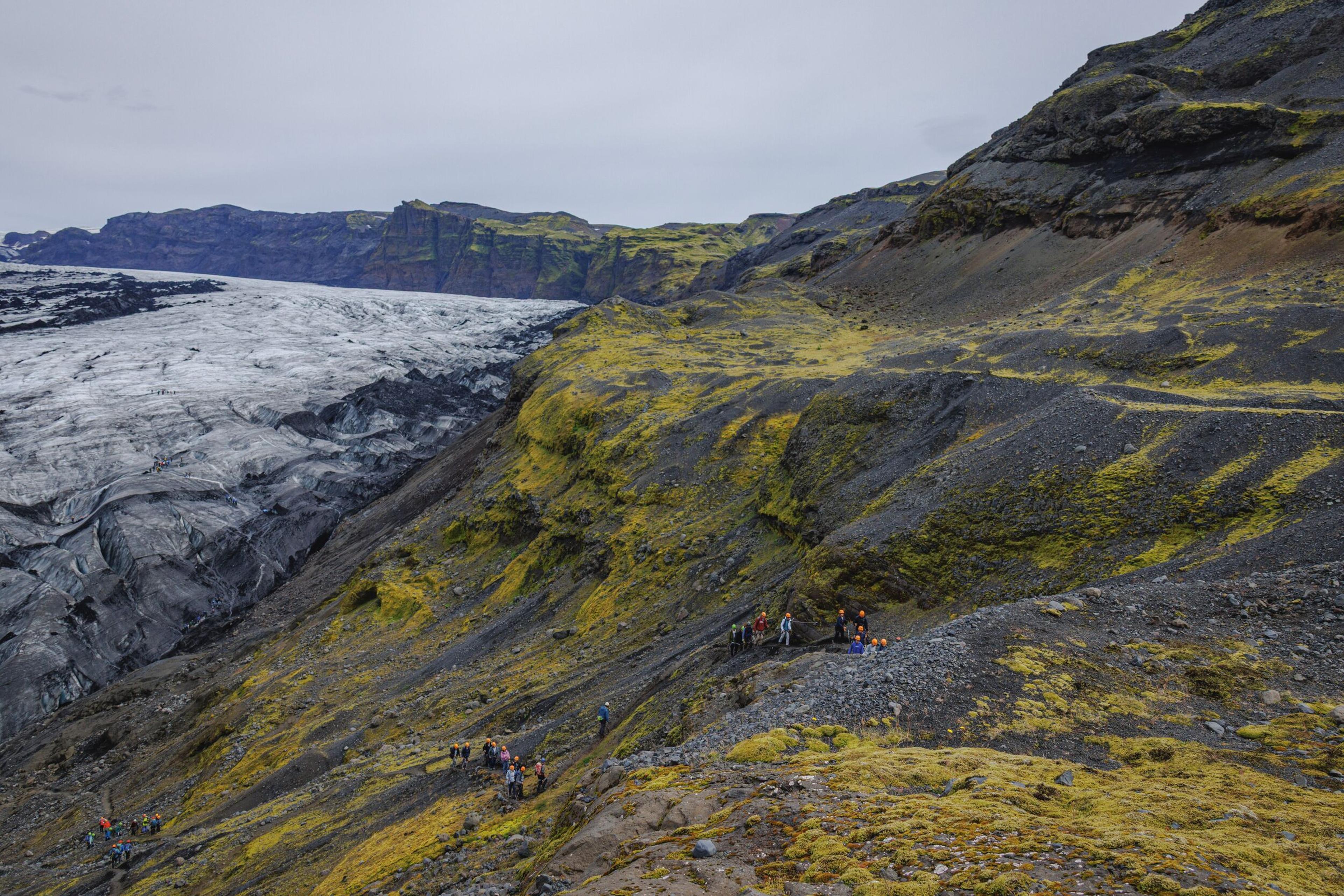A group of people on a rocky, moss-covered slope overlooking a large glacier.