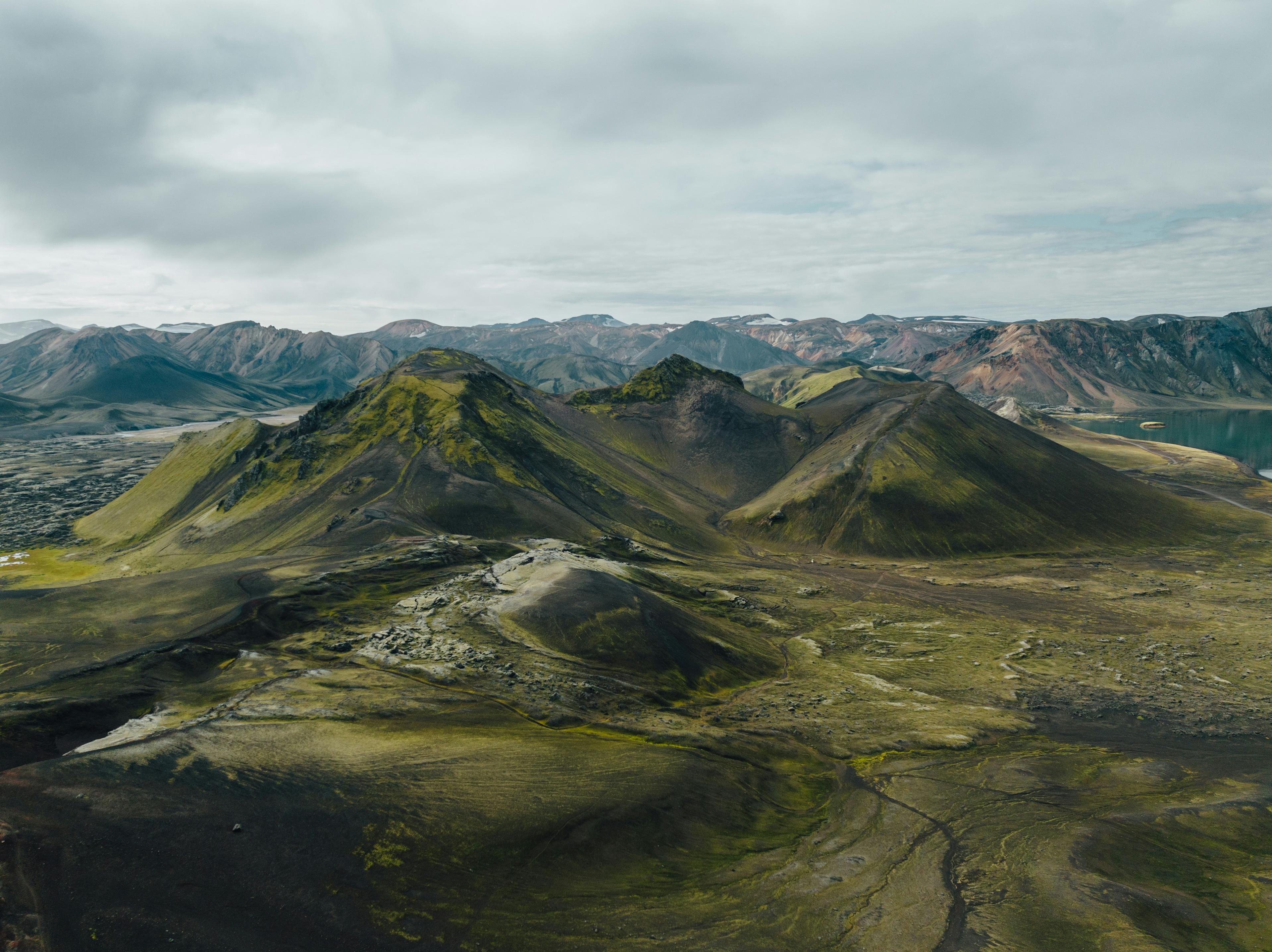 Aerial view of the Icelandic Highlands featuring moss-covered hills, rugged terrain, and distant mountain ranges under a cloudy sky.