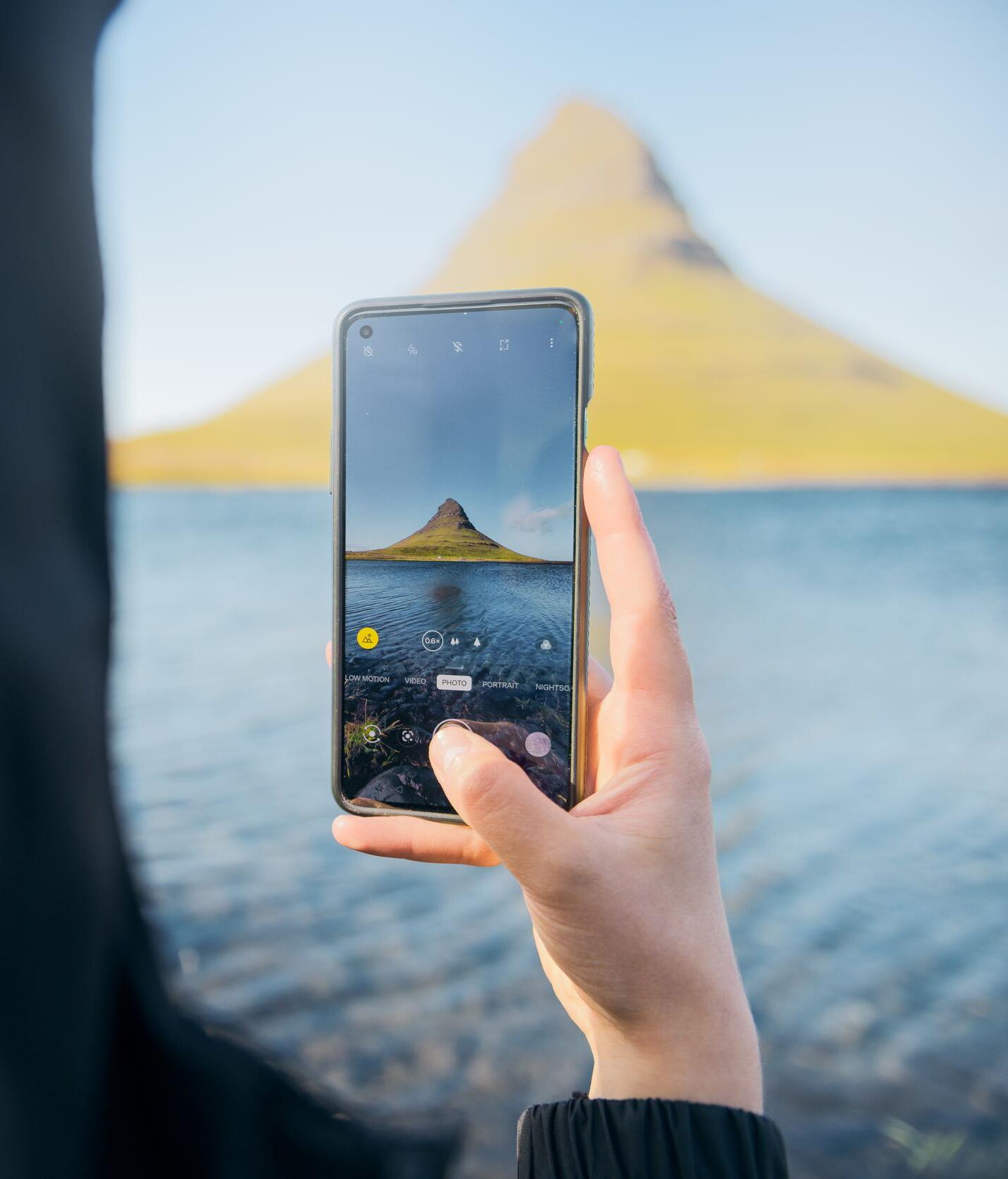 Woman in a blue knitted hat capturing a natural pool on her phone.