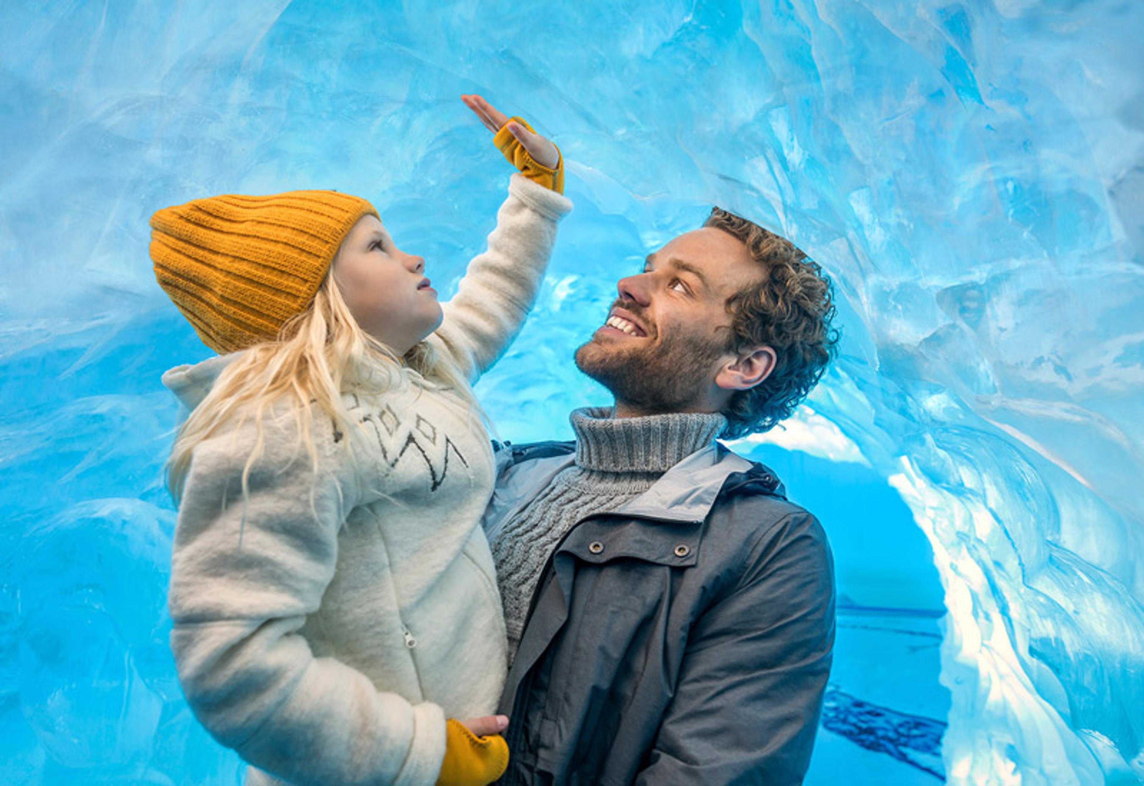 A father and daughter exploring the Perlan Ice Cave in Iceland, surrounded by stunning blue ice formations.