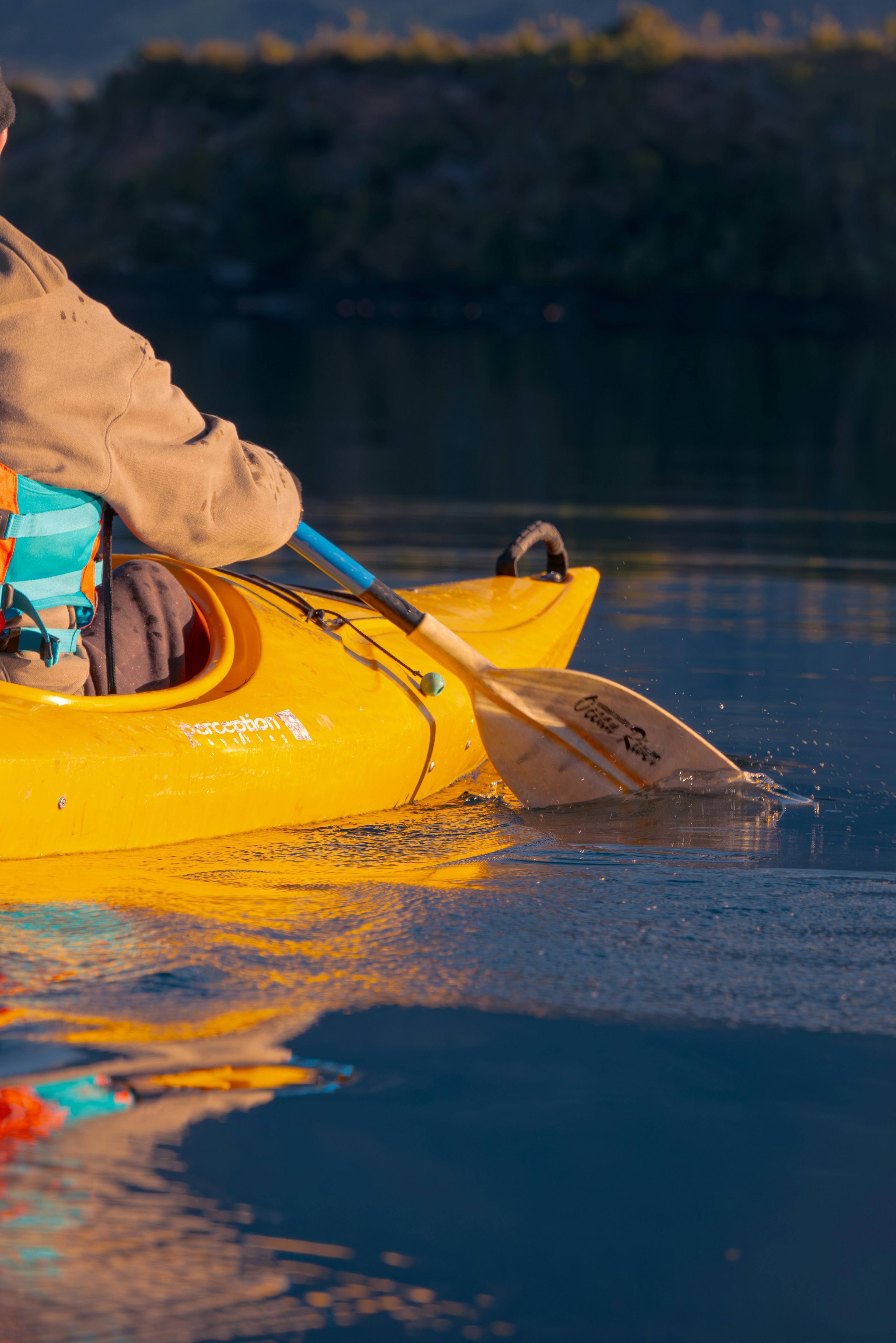 Close-up of a person paddling a yellow kayak on calm water during sunset, ideal for kayaking in Iceland.