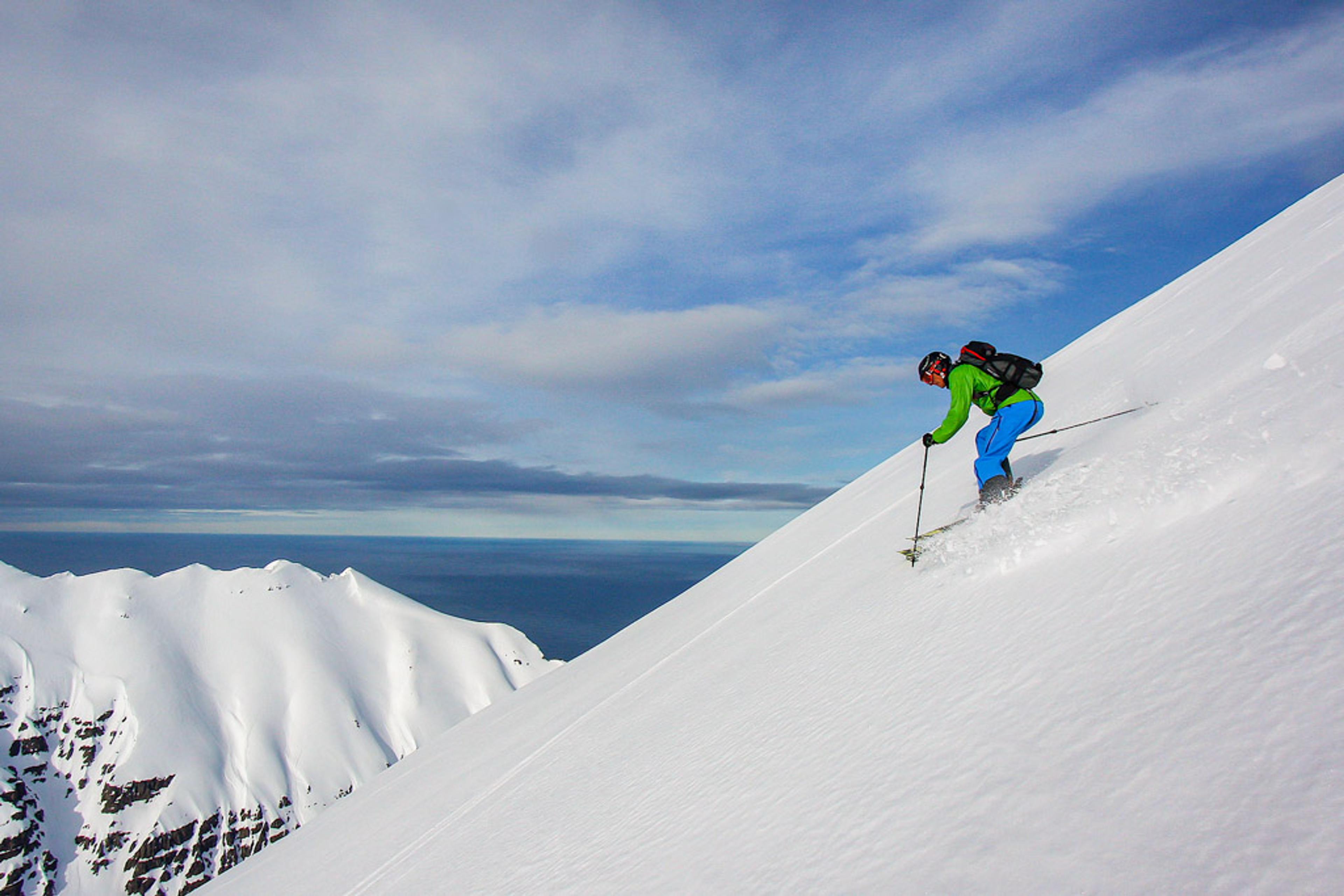 A skier gliding down a steep mountain with the ocean in the background