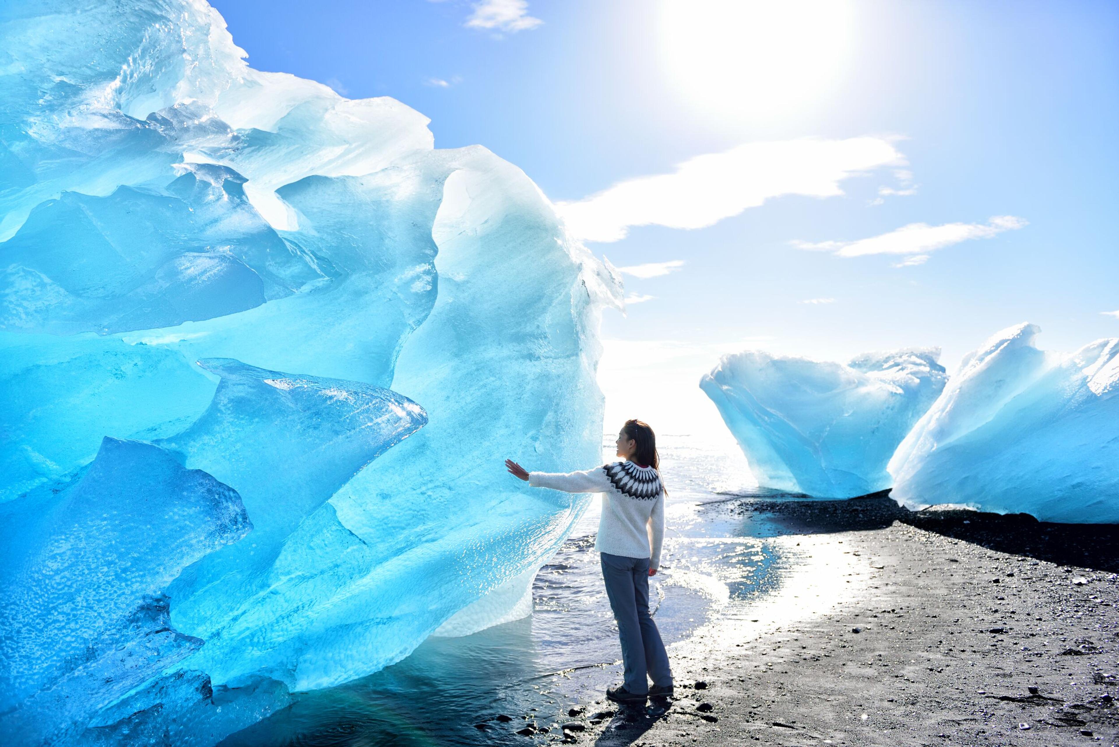 A person standing by an iceberg by the diamond beach shore in the soucth coast of Iceland.