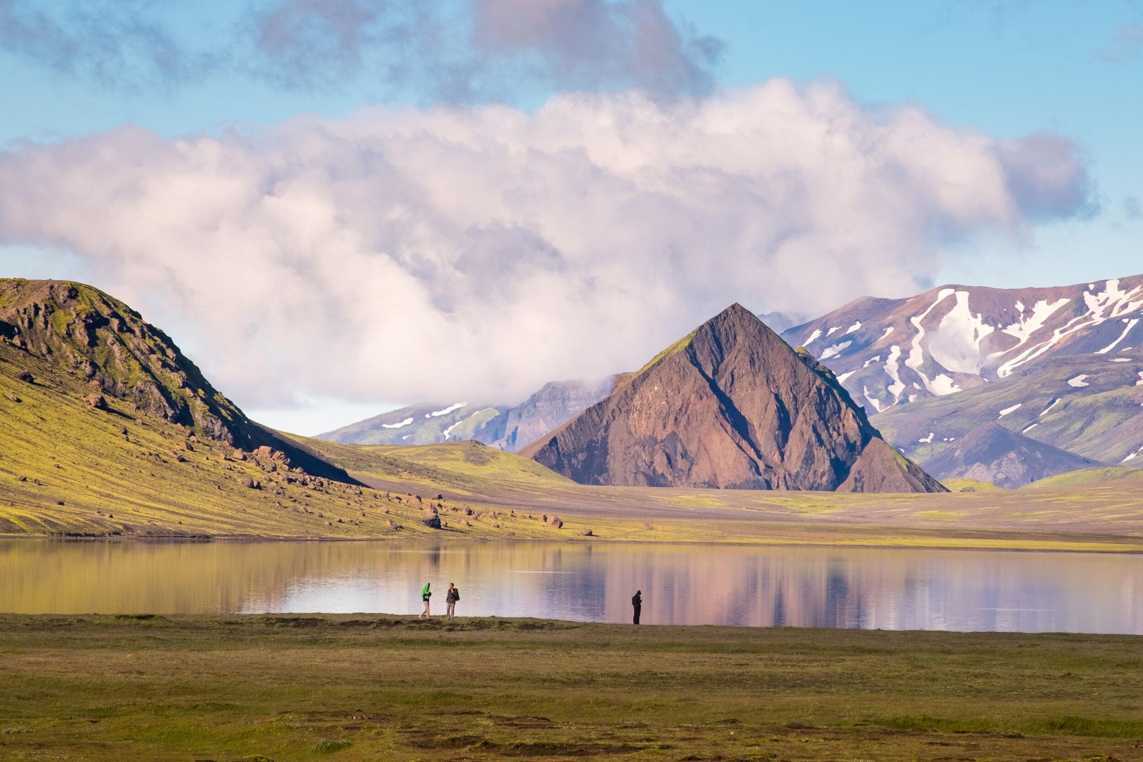 Hikers amidst a serene natural landscape, with a tranquil lake and a prominent mountain rising in the background.
