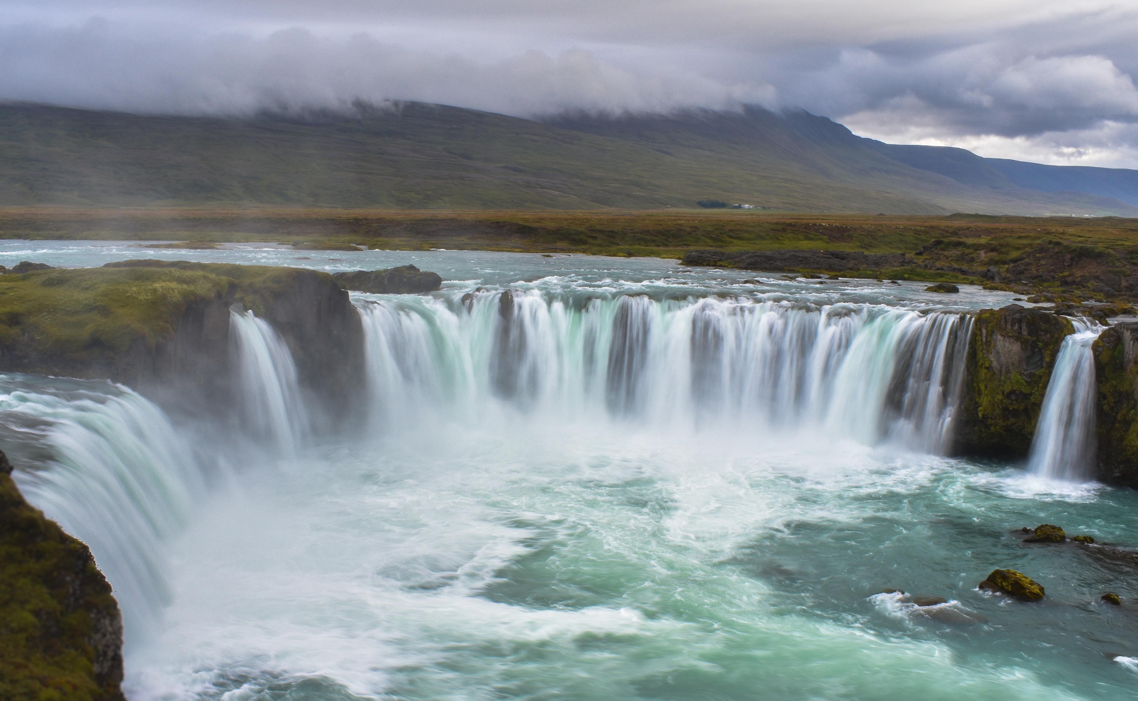 A horseshoe shaped waterfall with mountains in the background, on a foggy day