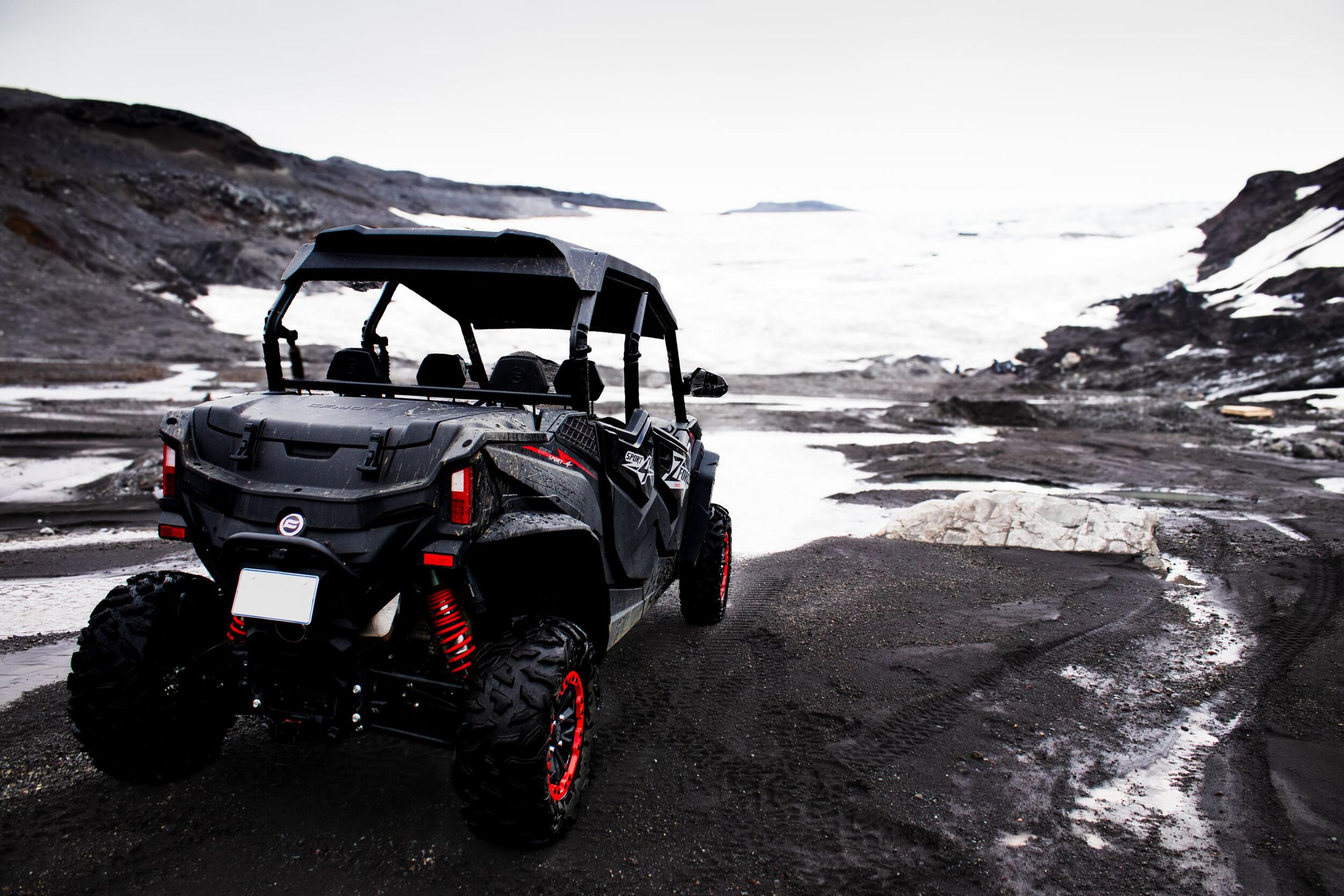 Black and red off-road vehicle on rocky terrain near a snow-covered landscape, ready for an adventure.