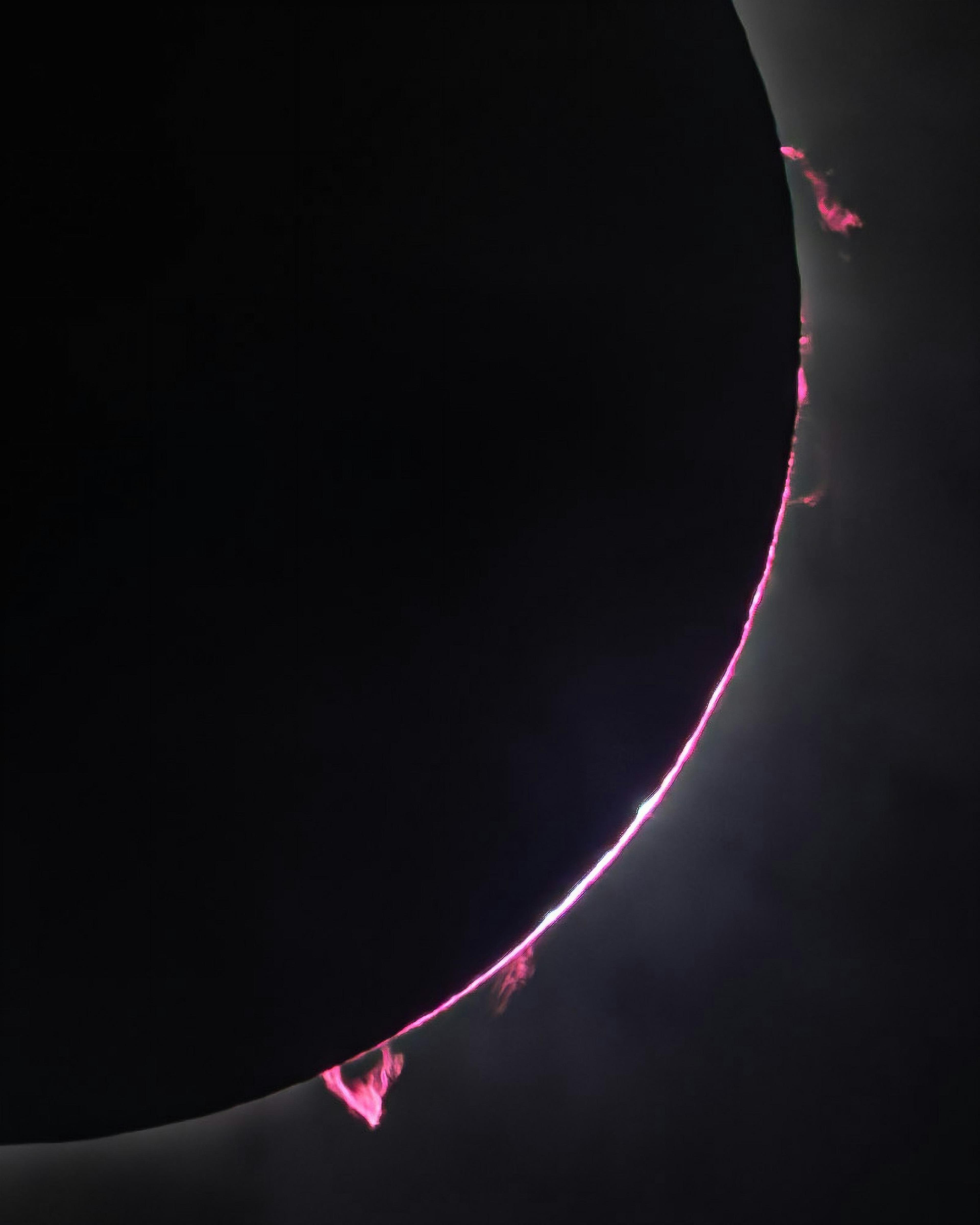 A total solar eclipse with the moon completely obscuring the sun, revealing bright pink solar flares along the sun's edge.