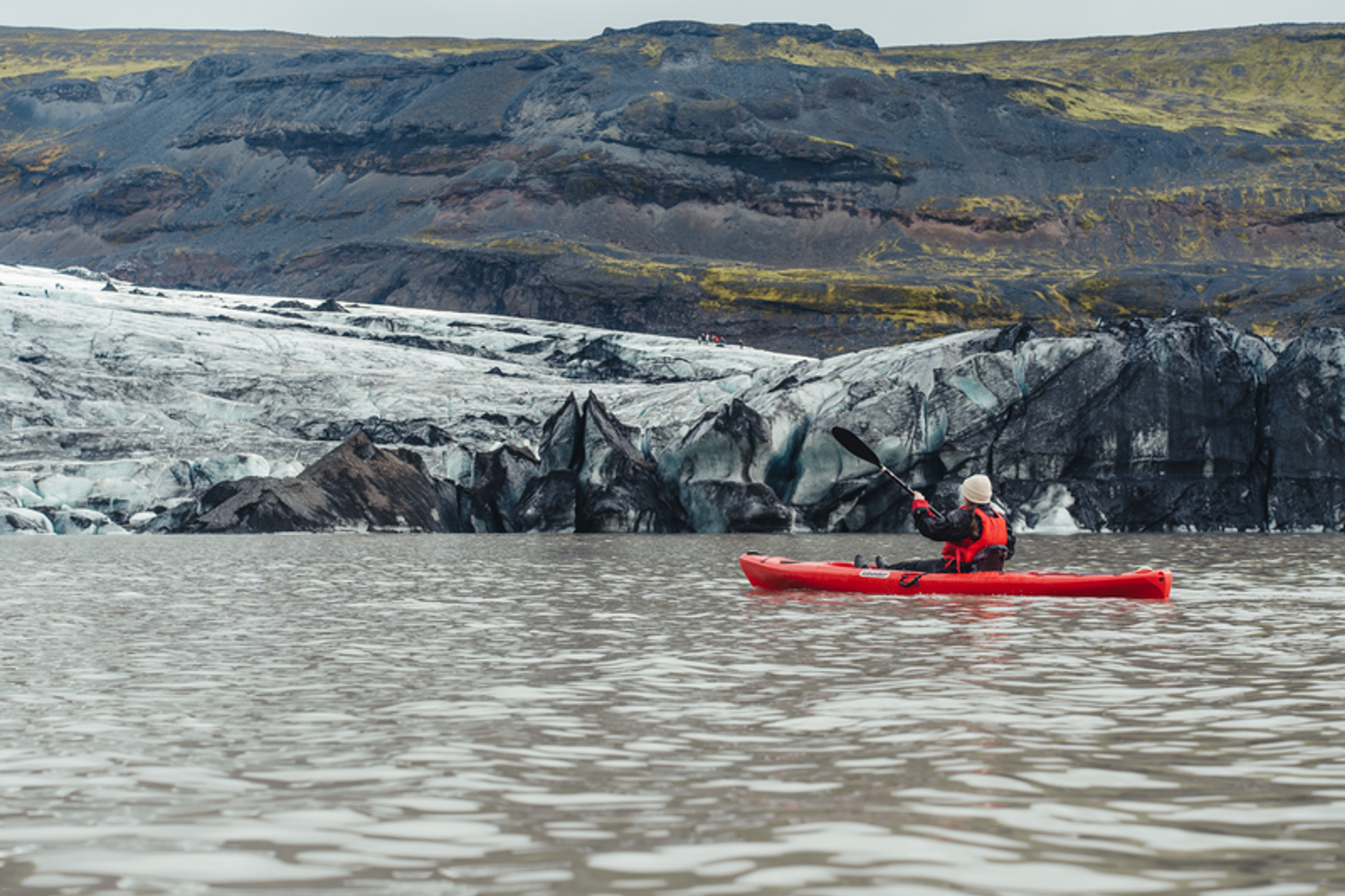 a man in a red kayak is paddling in front of a mountain