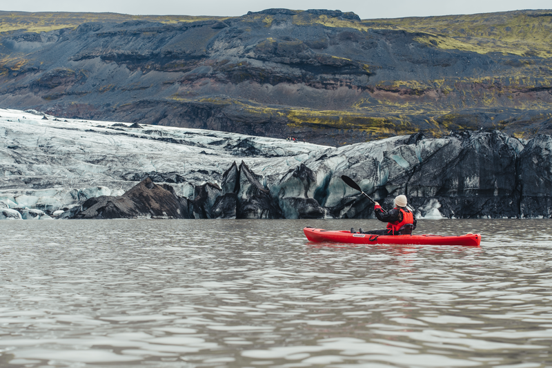 a man in a red kayak is paddling in front of a mountain