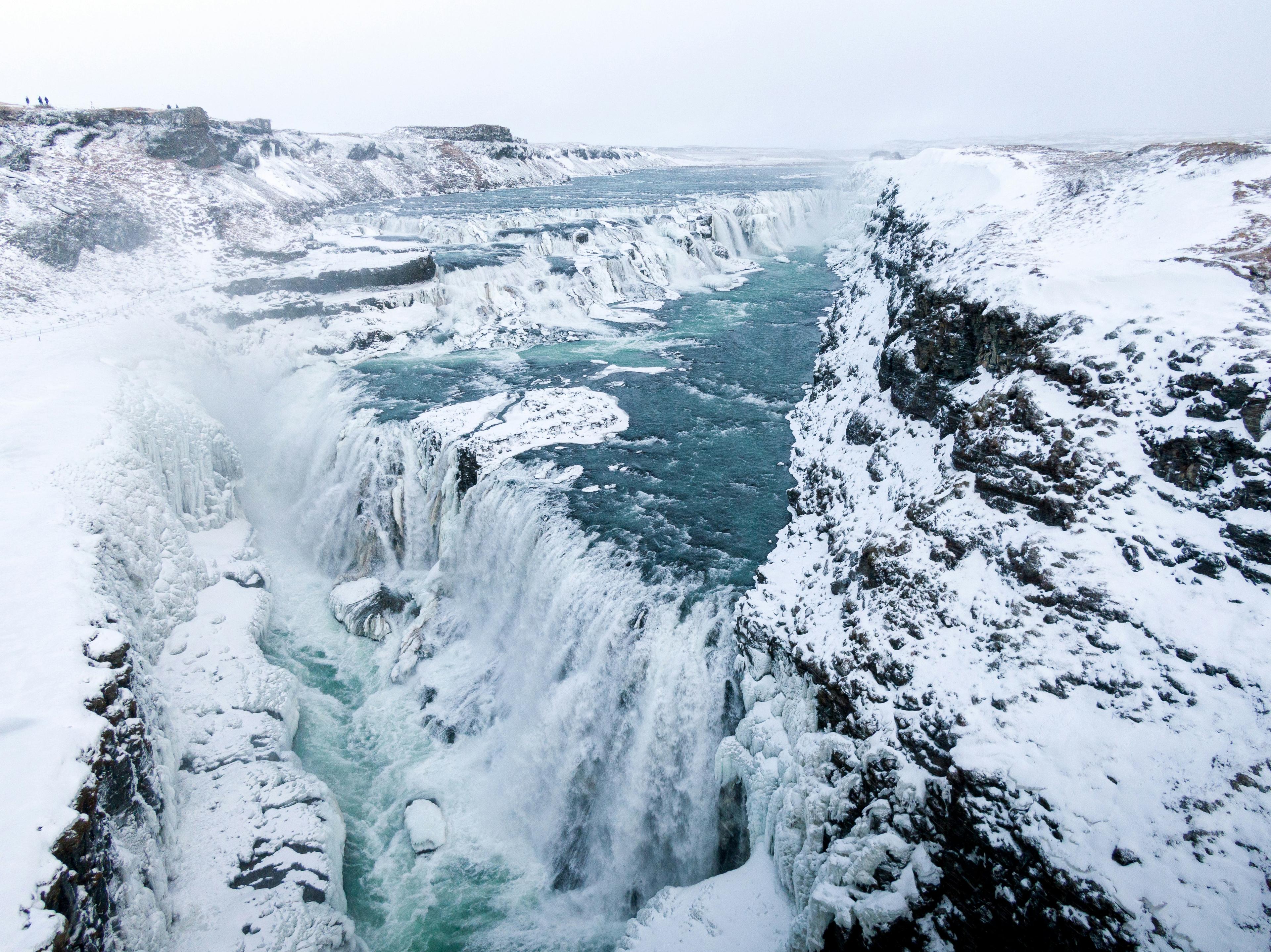 A wide, multi-tiered waterfall surrounded by snow-covered cliffs, its icy waters flowing through a rugged landscape, evoking the serene and frosty beauty of Iceland's natural wonders.
