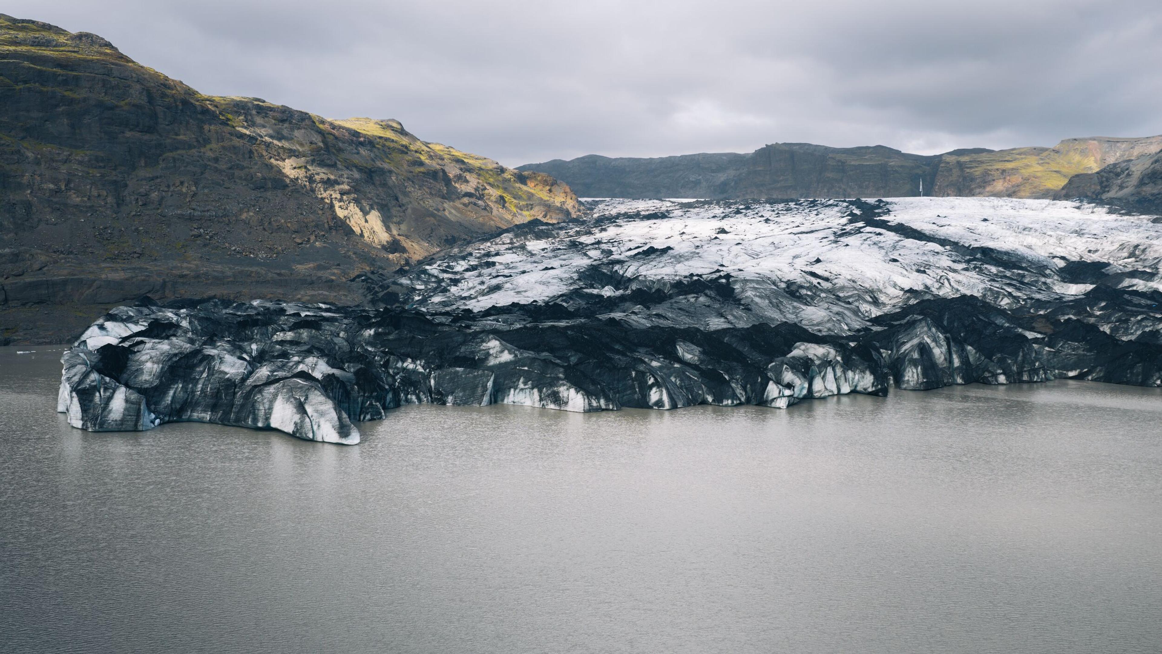 a large iceberg is floating in the middle of a lake surrounded by mountains .
