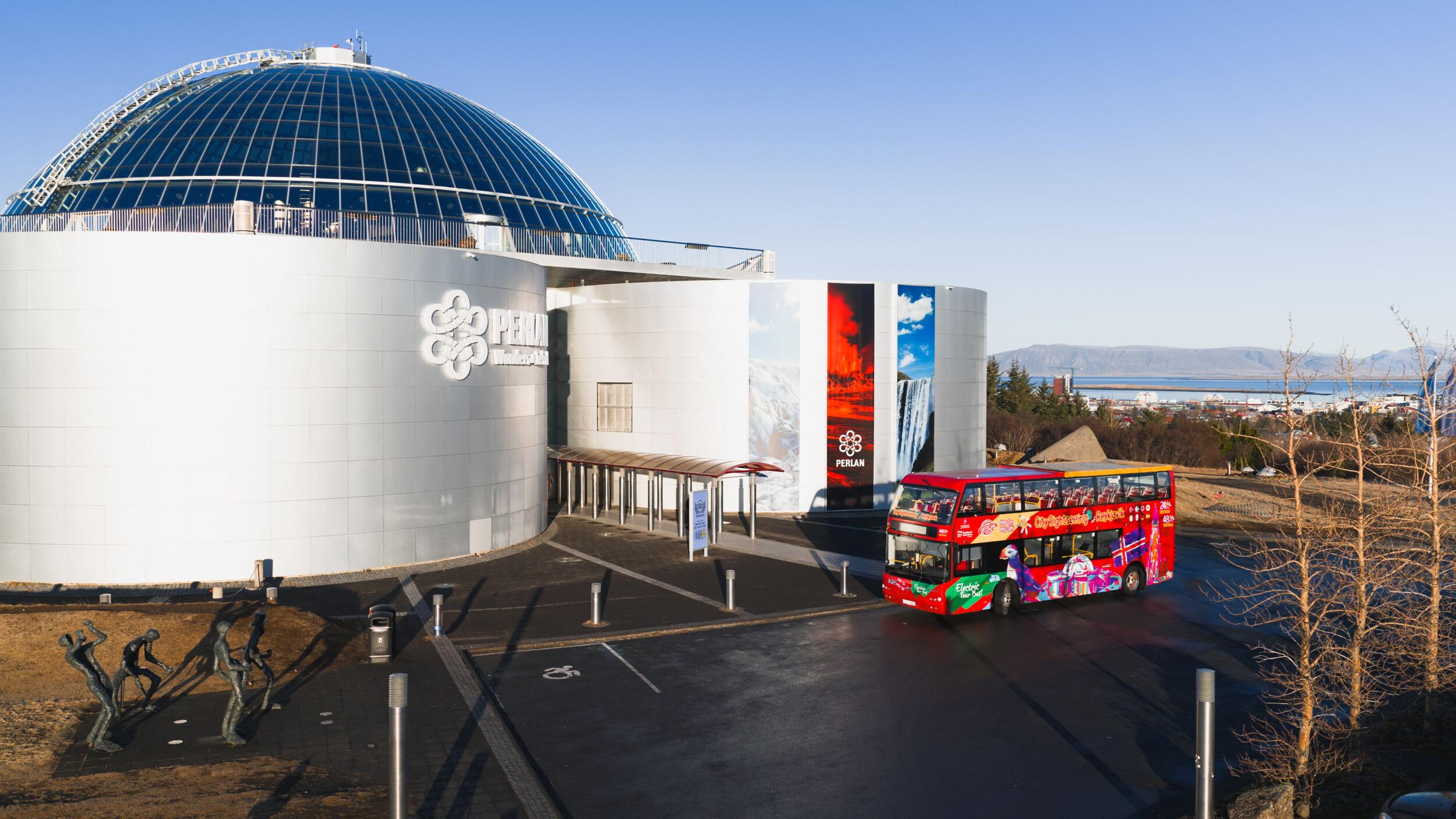 The Perlan building with a glass dome and a colorful red double-decker tour bus parked in front.