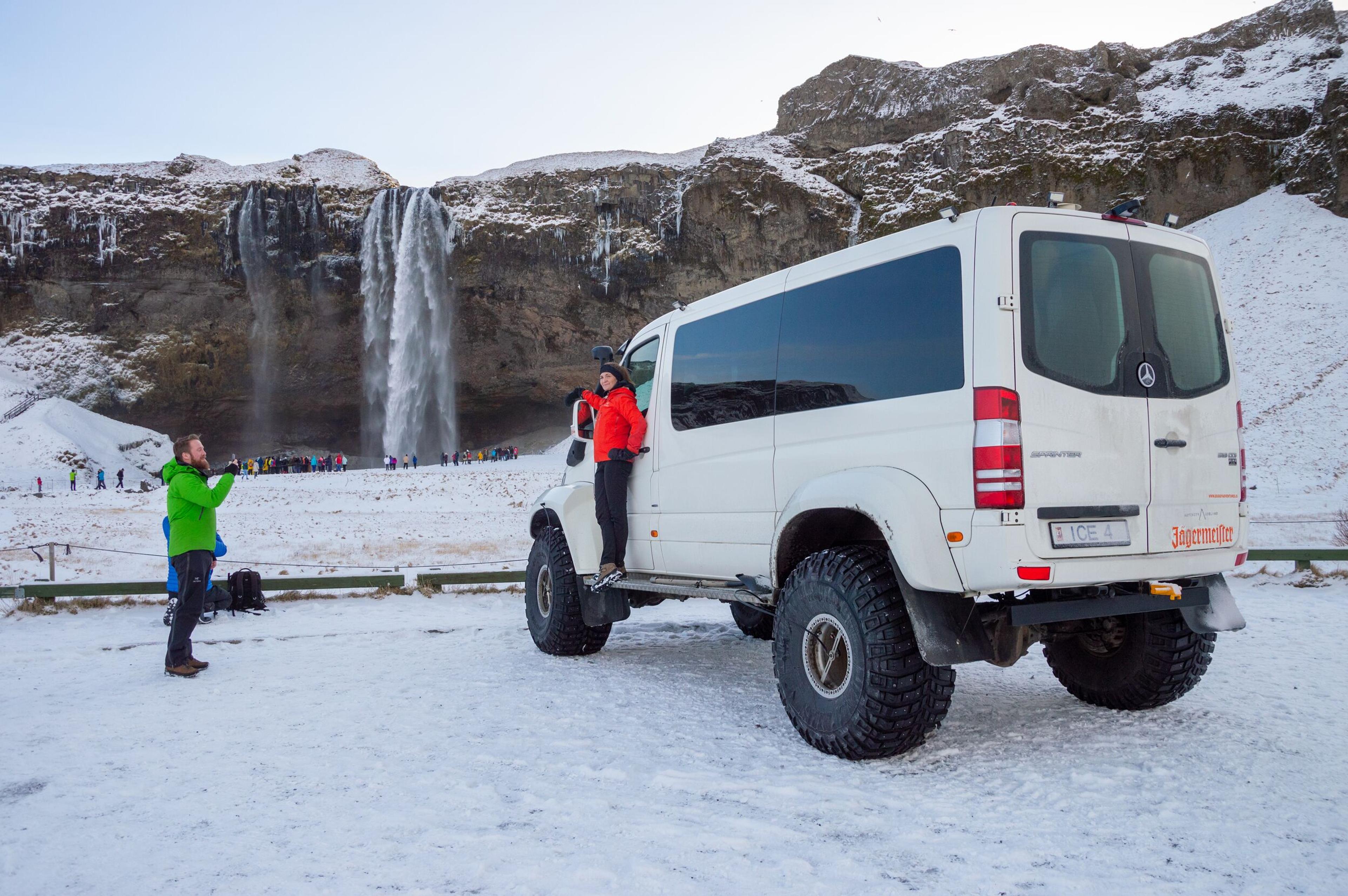 tourists on a super-jepp by Seljalandsfoss waterfall during winter time.