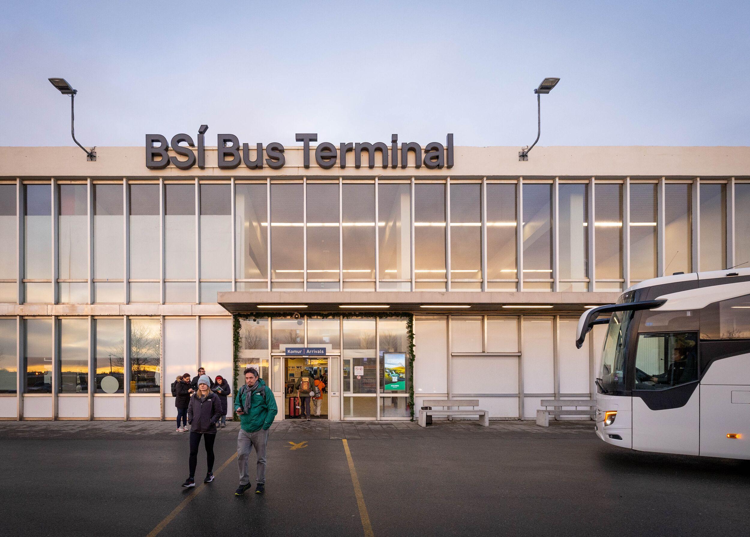 BSI Bus Terminal building with people walking outside and a white bus parked nearby.