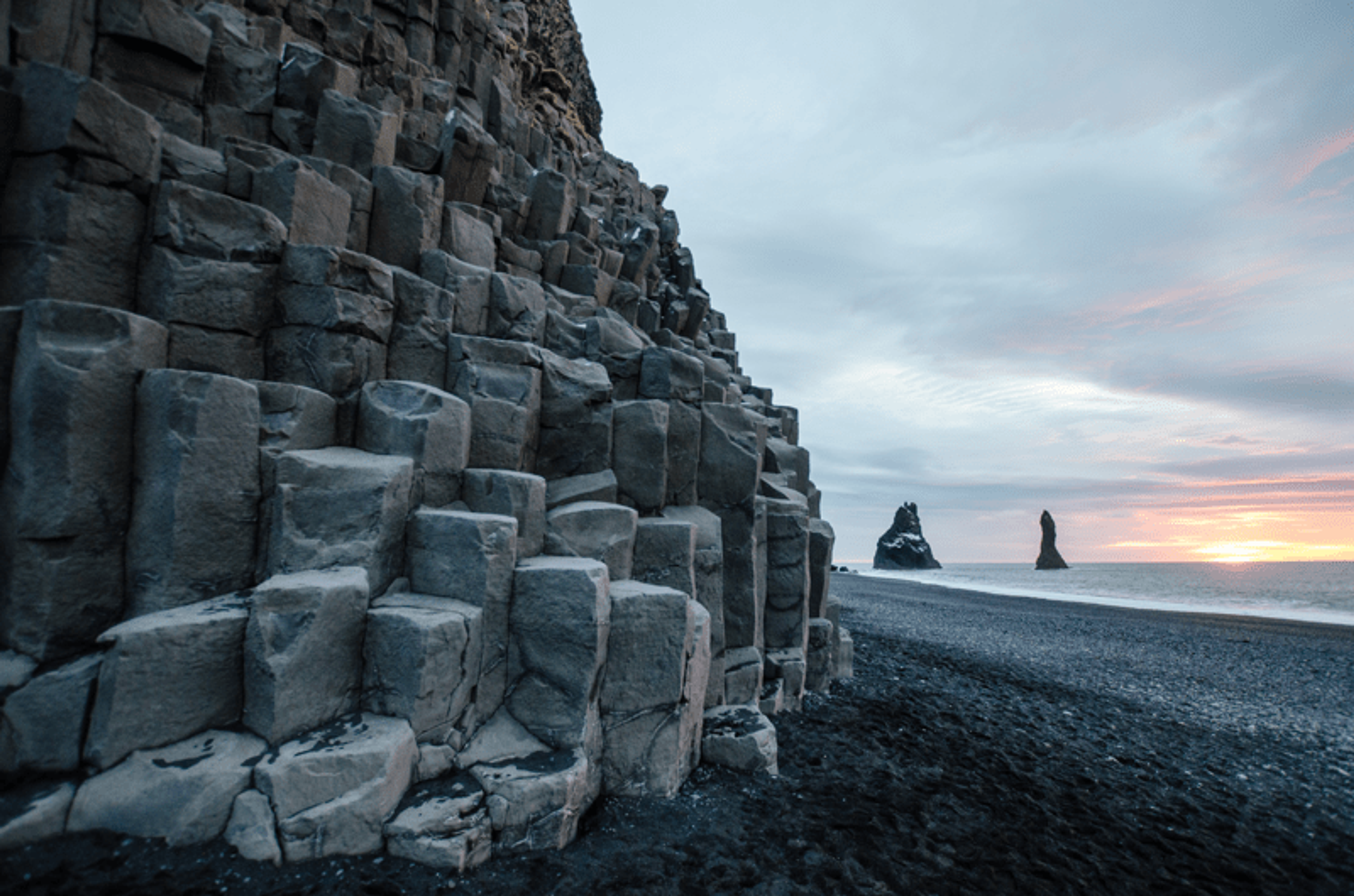 Black sand beach with hexagonal basalt columns, sea stacks, and a sunset.