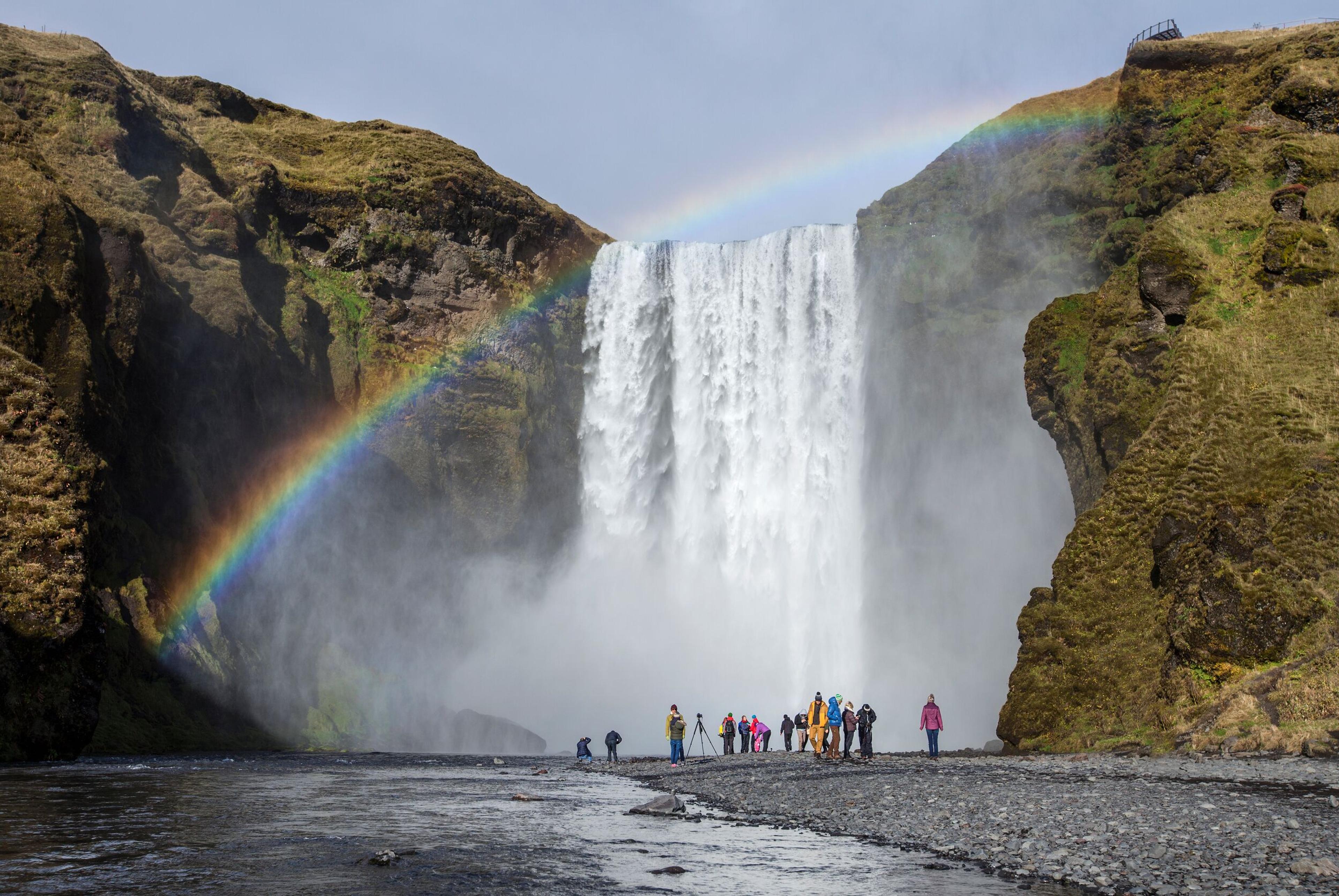 A group of people at the bottom of the Skógafoss Waterfall in the south coast of Iceland. Striking rainbow over the waterfall.