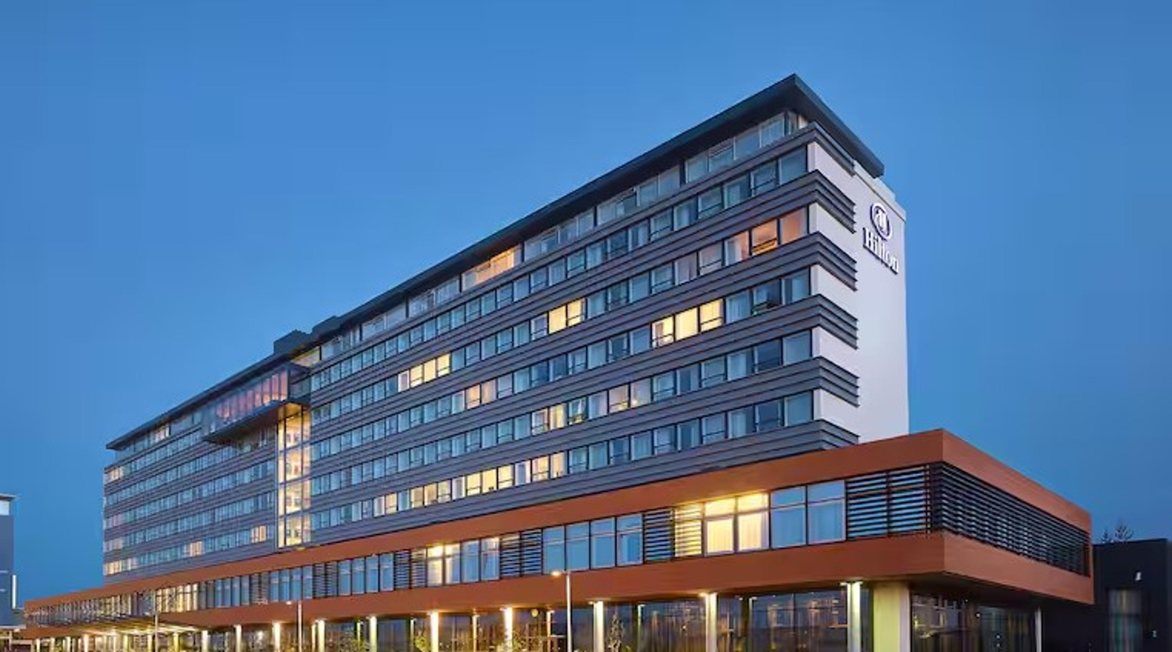 Modern Hilton hotel building in Reykjavik, illuminated at dusk against a clear sky.