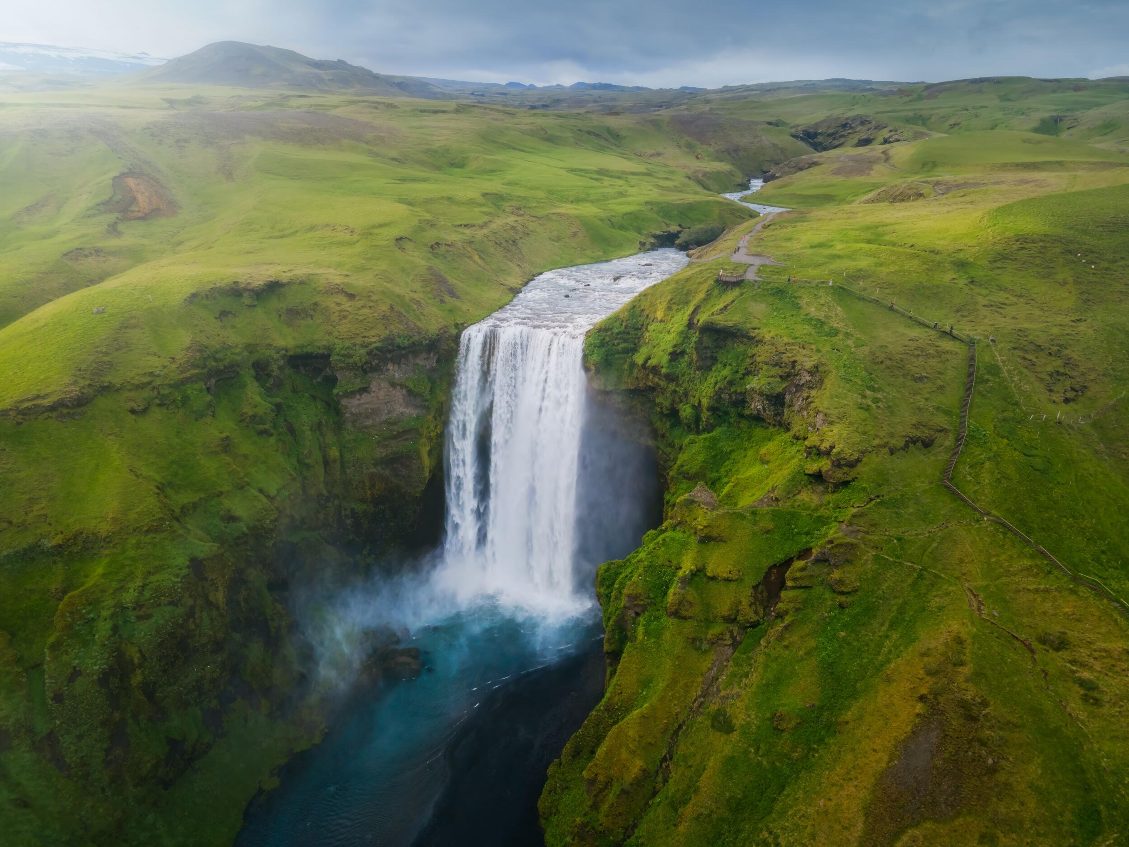 An aerial view of a majestic waterfall in a lush green landscape with a river running away from the fall towards the horizon.
