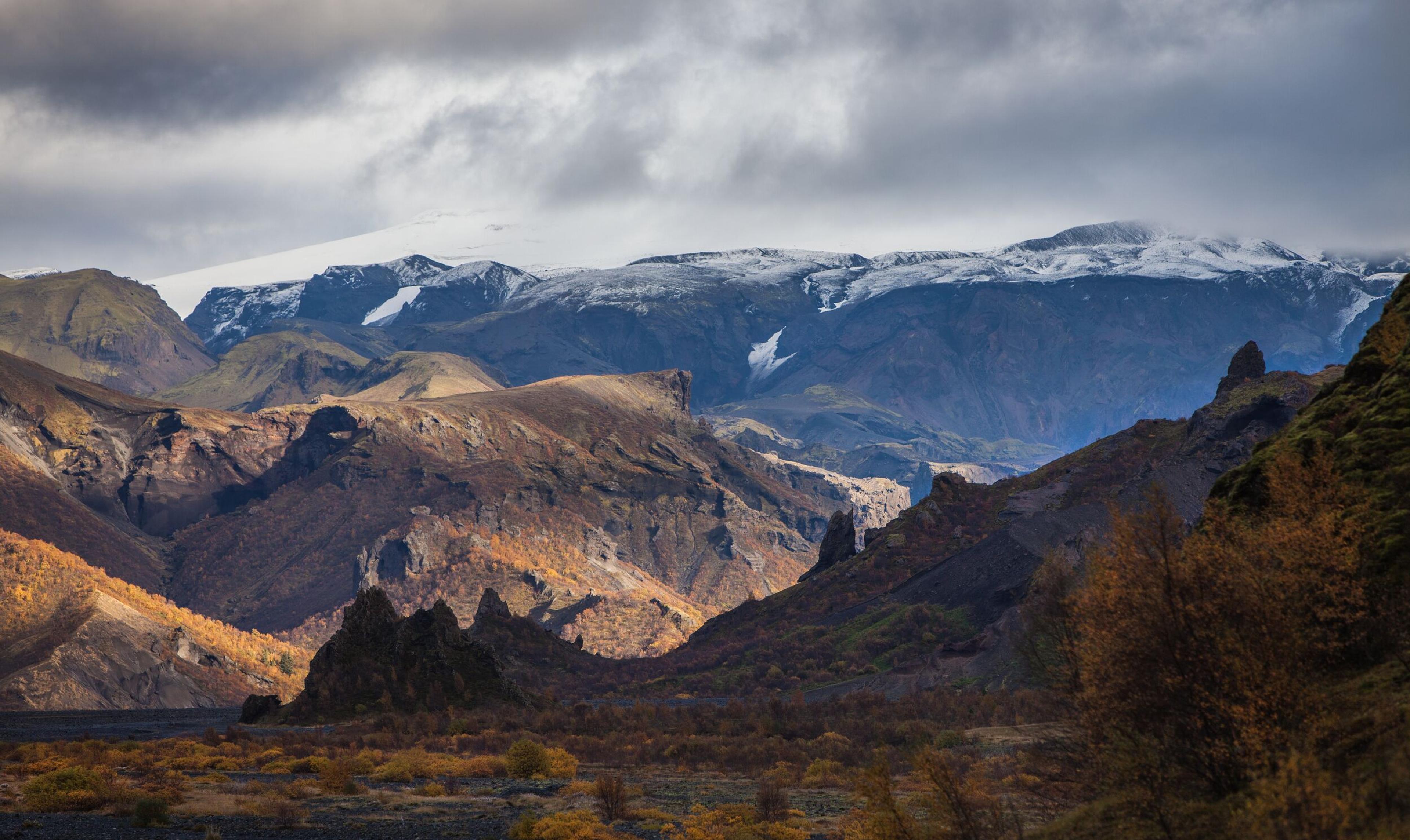 Majestic Icelandic landscape with rugged mountains, rocky formations, and snow-capped peaks under a cloudy sky.