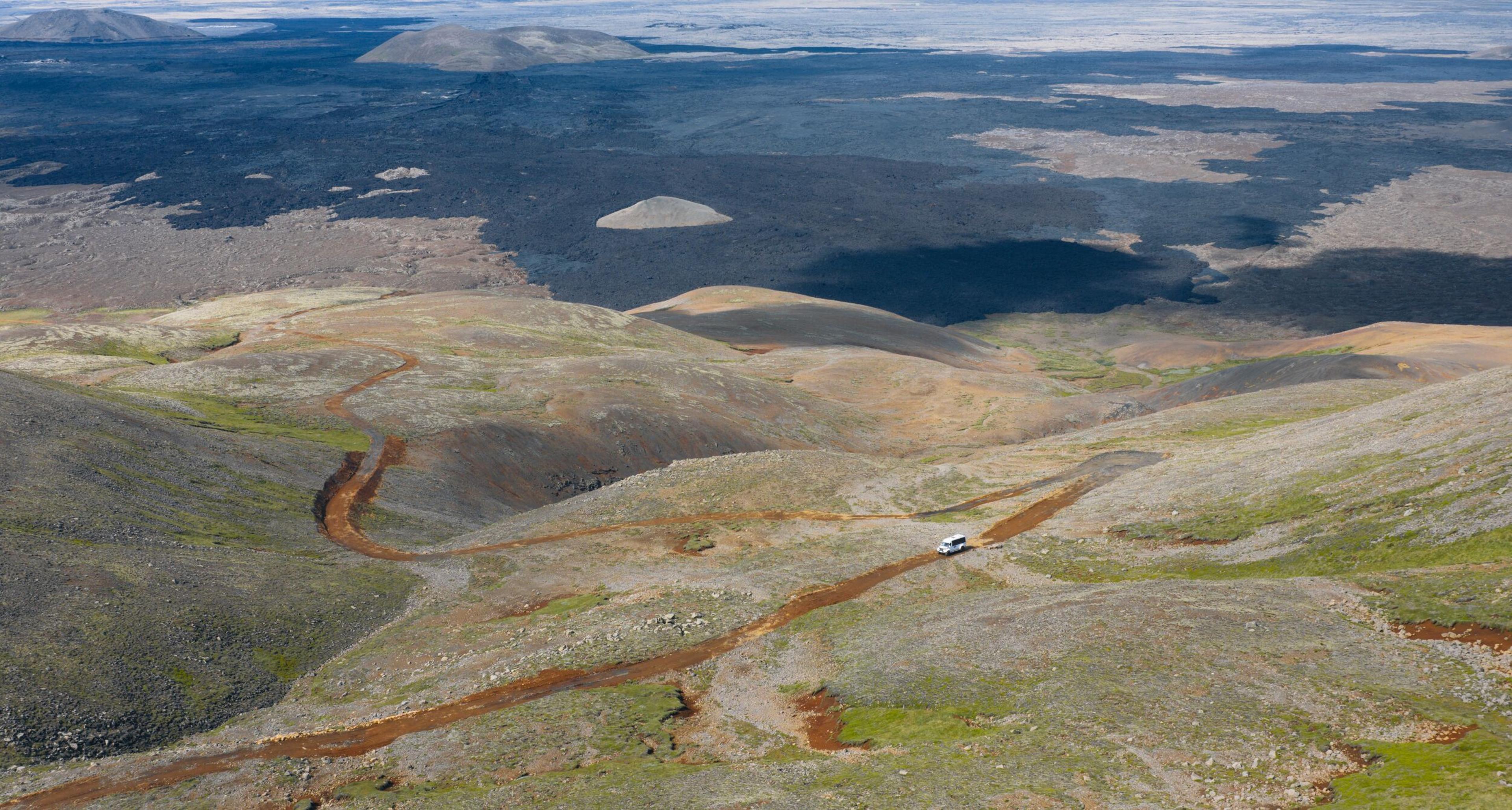 an aerial view of a car driving down a dirt road in the mountains .