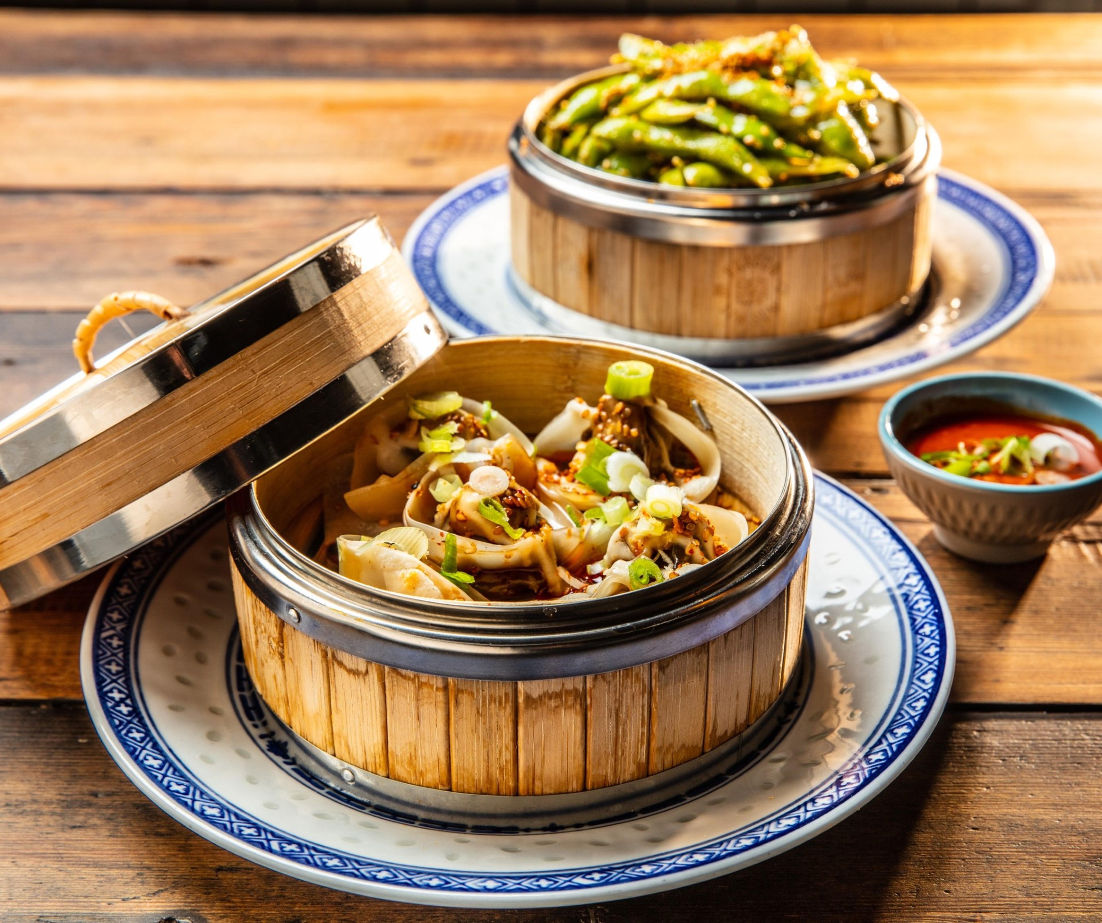 Close-up of delicious dumplings and green beans served in bamboo steamers, presented on decorative plates.