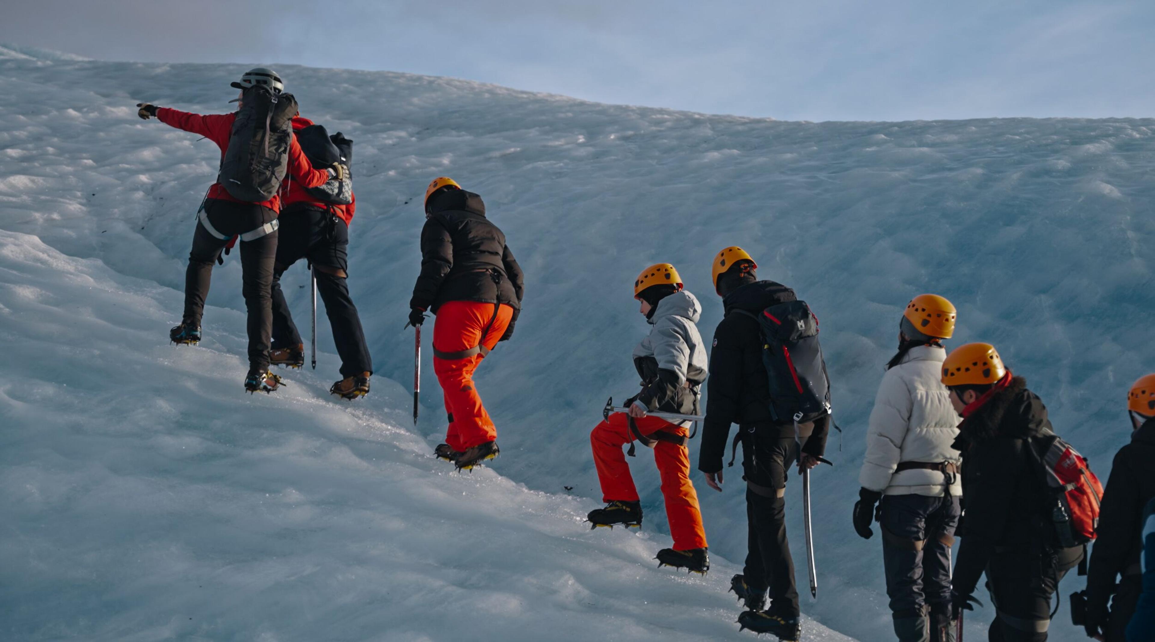 Glacier hikers with gear ascending an ice slope, one pointing ahead.
